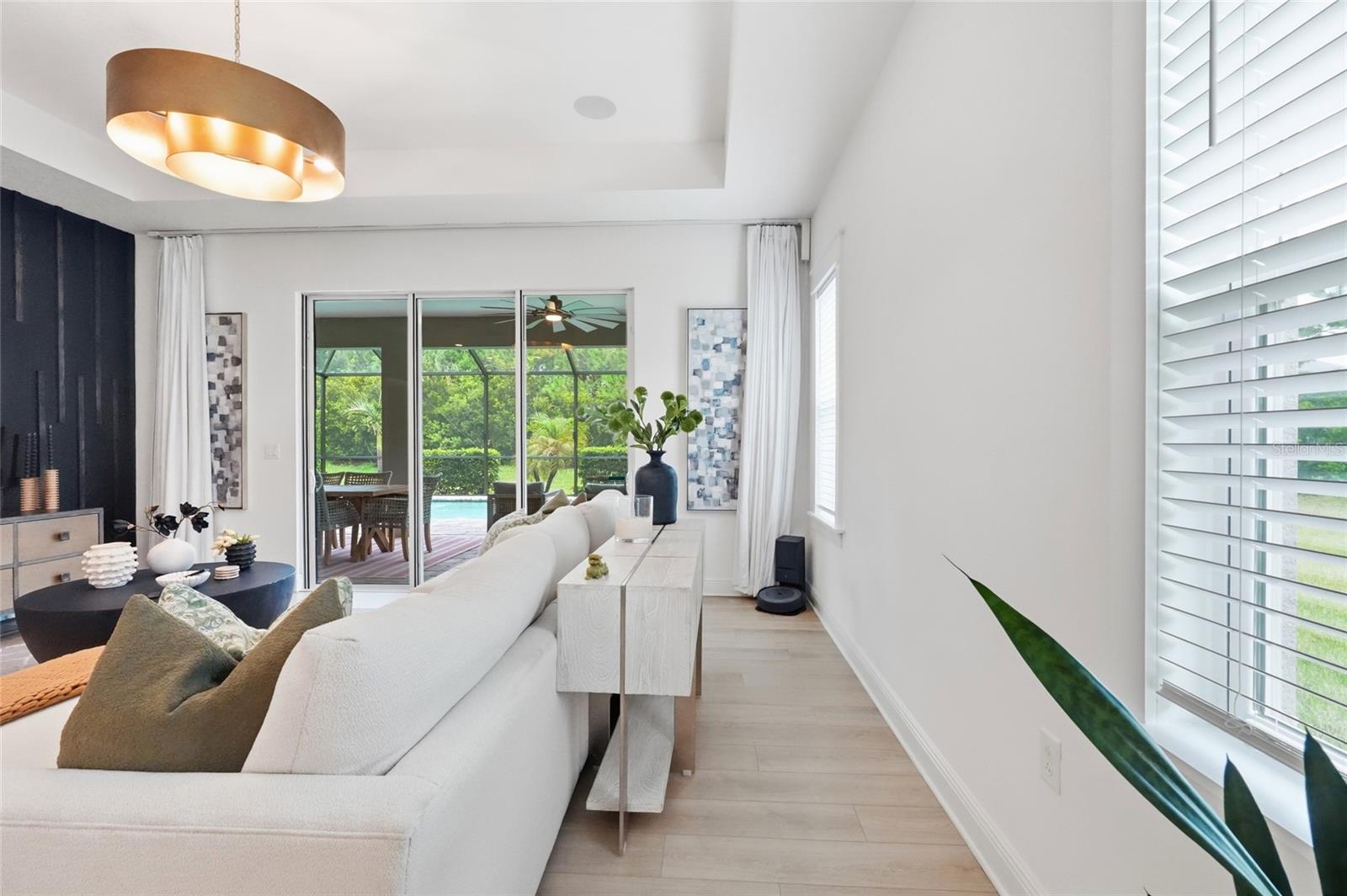 Staged living room with a white sectional and sliding doors overlooking a screened patio and pool.