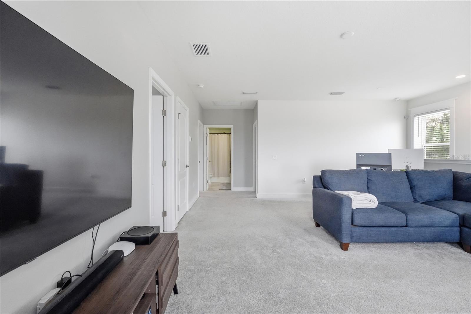 Living room with a blue sectional, wall-mounted television, and carpeted hallway.