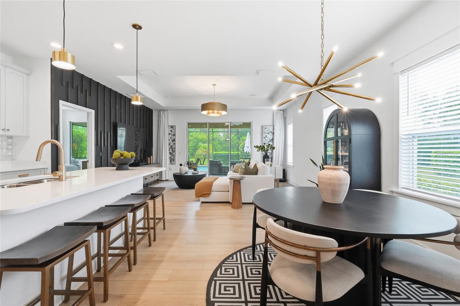 Open-plan kitchen and living room with a white island, dark paneled wall, and pool view through sliding doors.