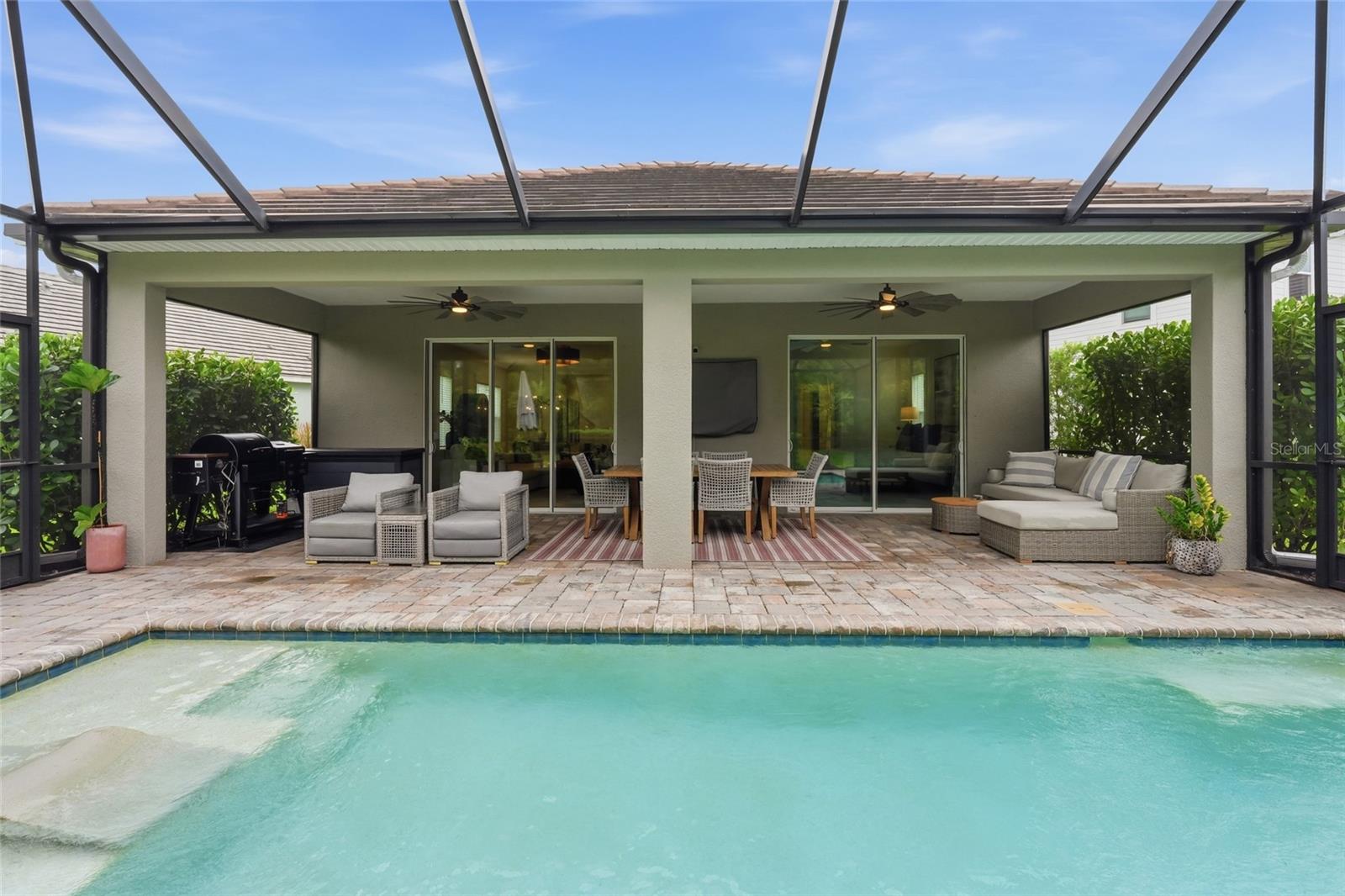Backyard pool beside a furnished covered lanai with outdoor dining and lounge seating.