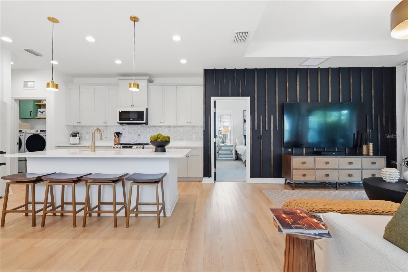 Open-plan kitchen and living room with a white island, bar stools, and a dark TV accent wall.
