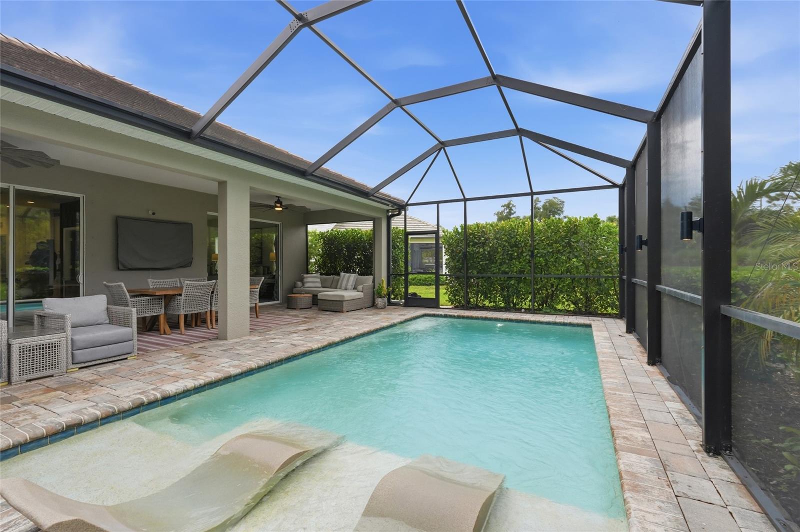 Backyard pool with a shallow tanning ledge, screened enclosure, and furnished covered patio.