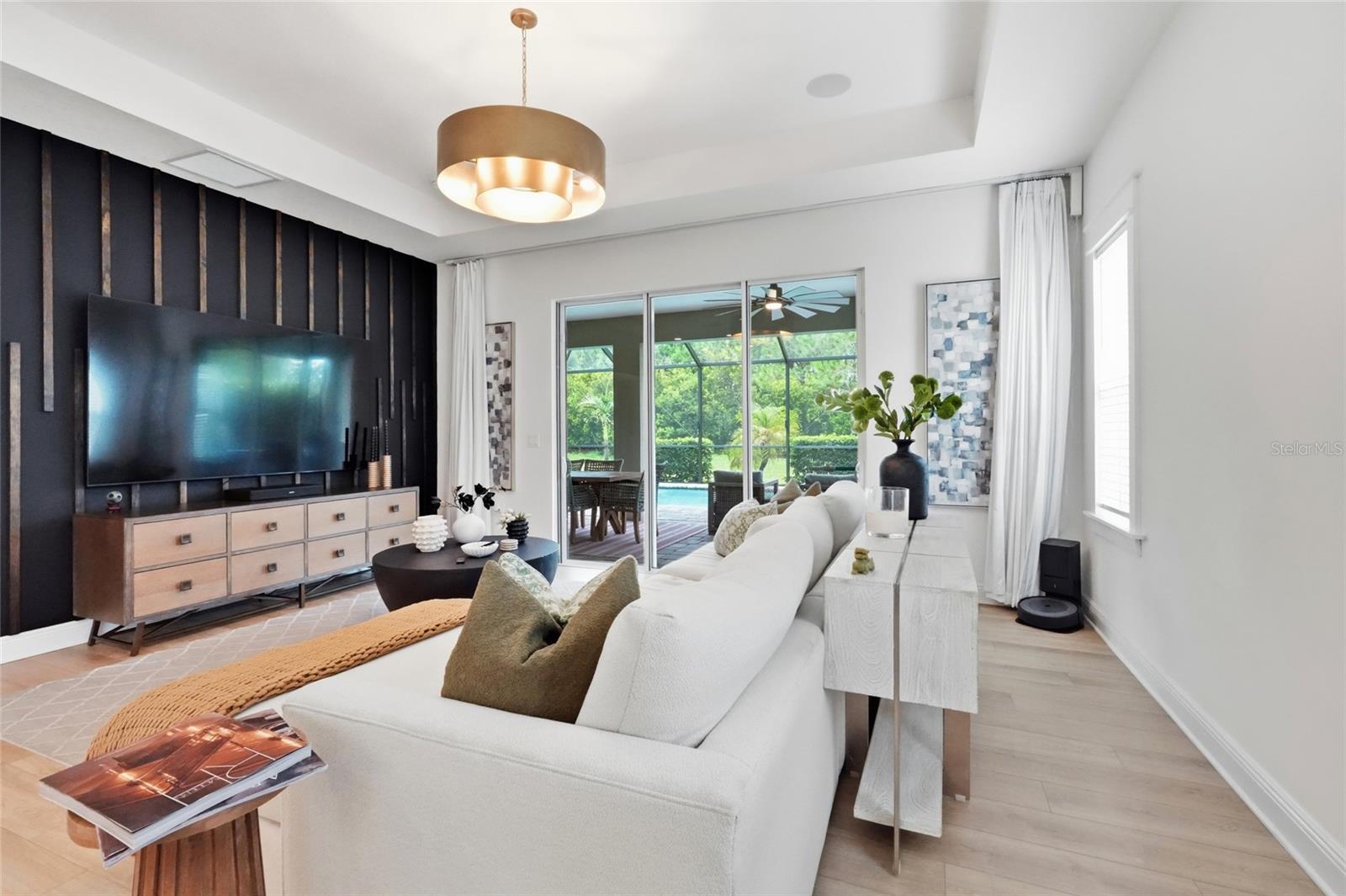 Living room with a white sectional, dark TV wall, and sliding doors overlooking the pool.