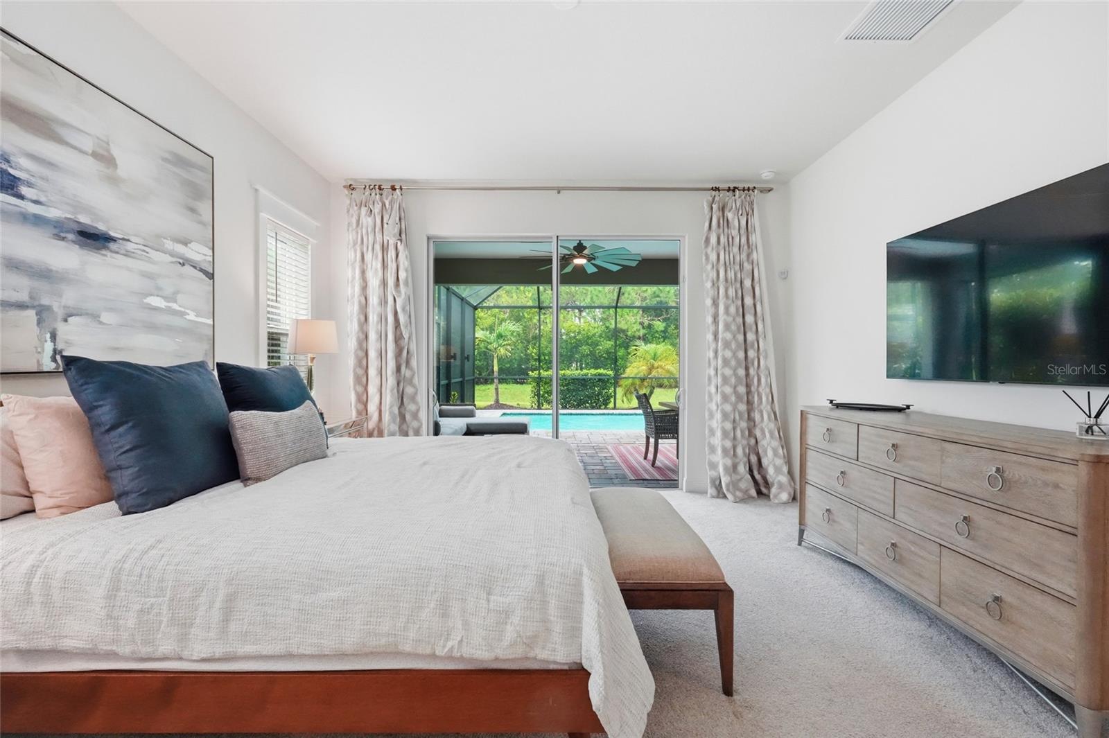 Furnished bedroom with sliding glass doors overlooking a screened pool patio and greenery.