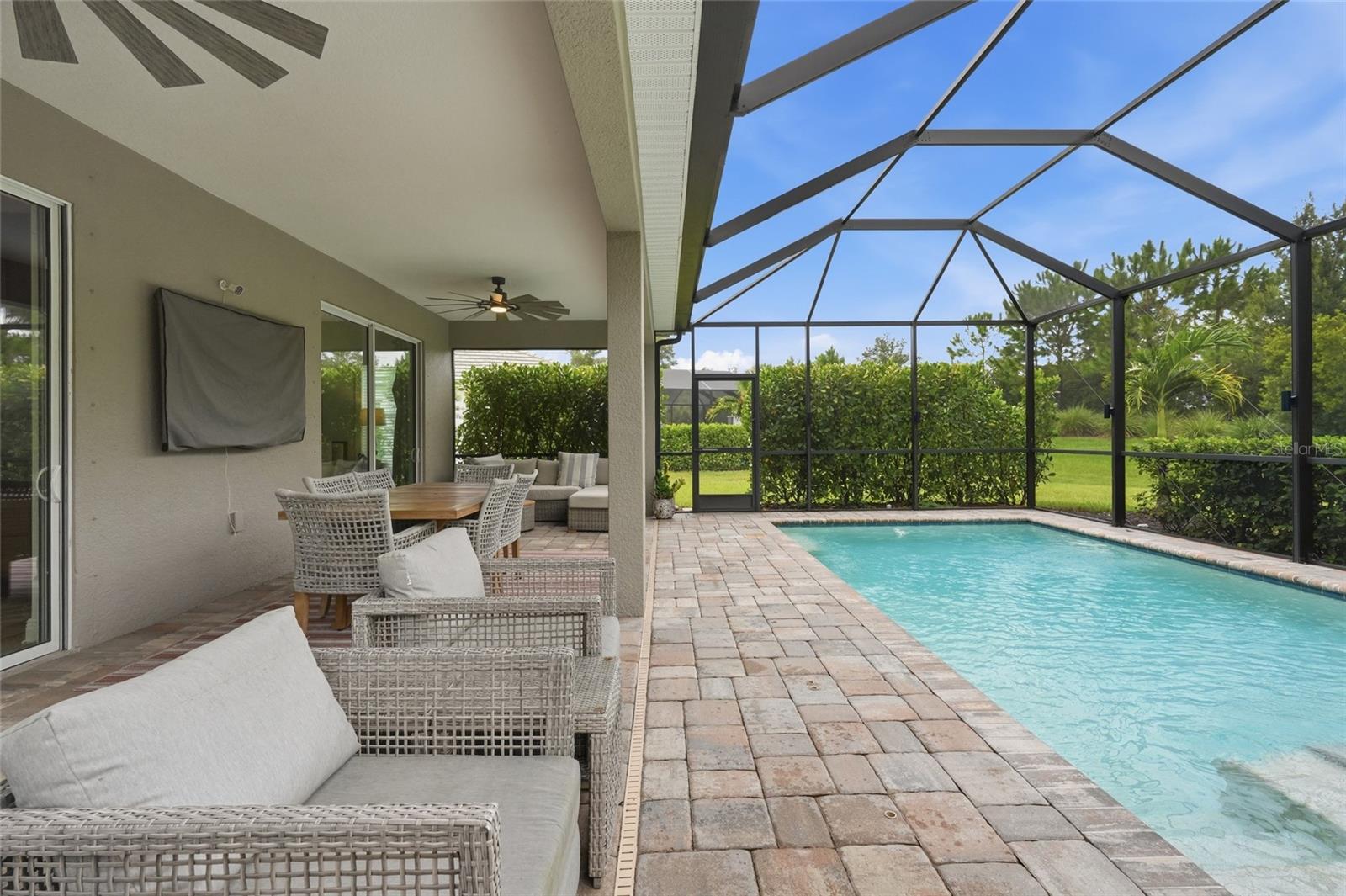 Screened backyard pool beside a covered patio furnished with wicker seating and an outdoor dining table.