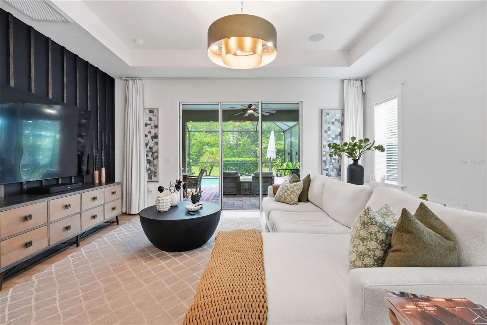 Furnished living room with a white sectional, dramatic black media wall, and sliding doors to a screened lanai.