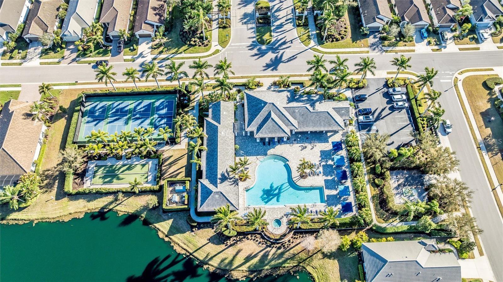 Aerial view of a lakeside home with a pool, tennis courts, and landscaped grounds.