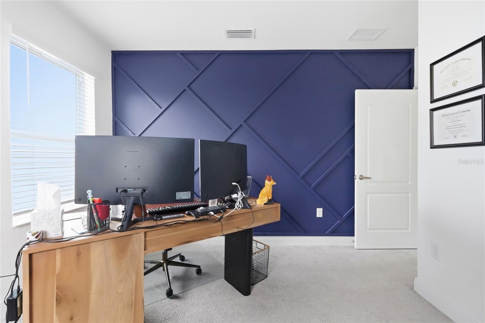 Home office with a navy geometric accent wall, wooden desk, and dual monitors.