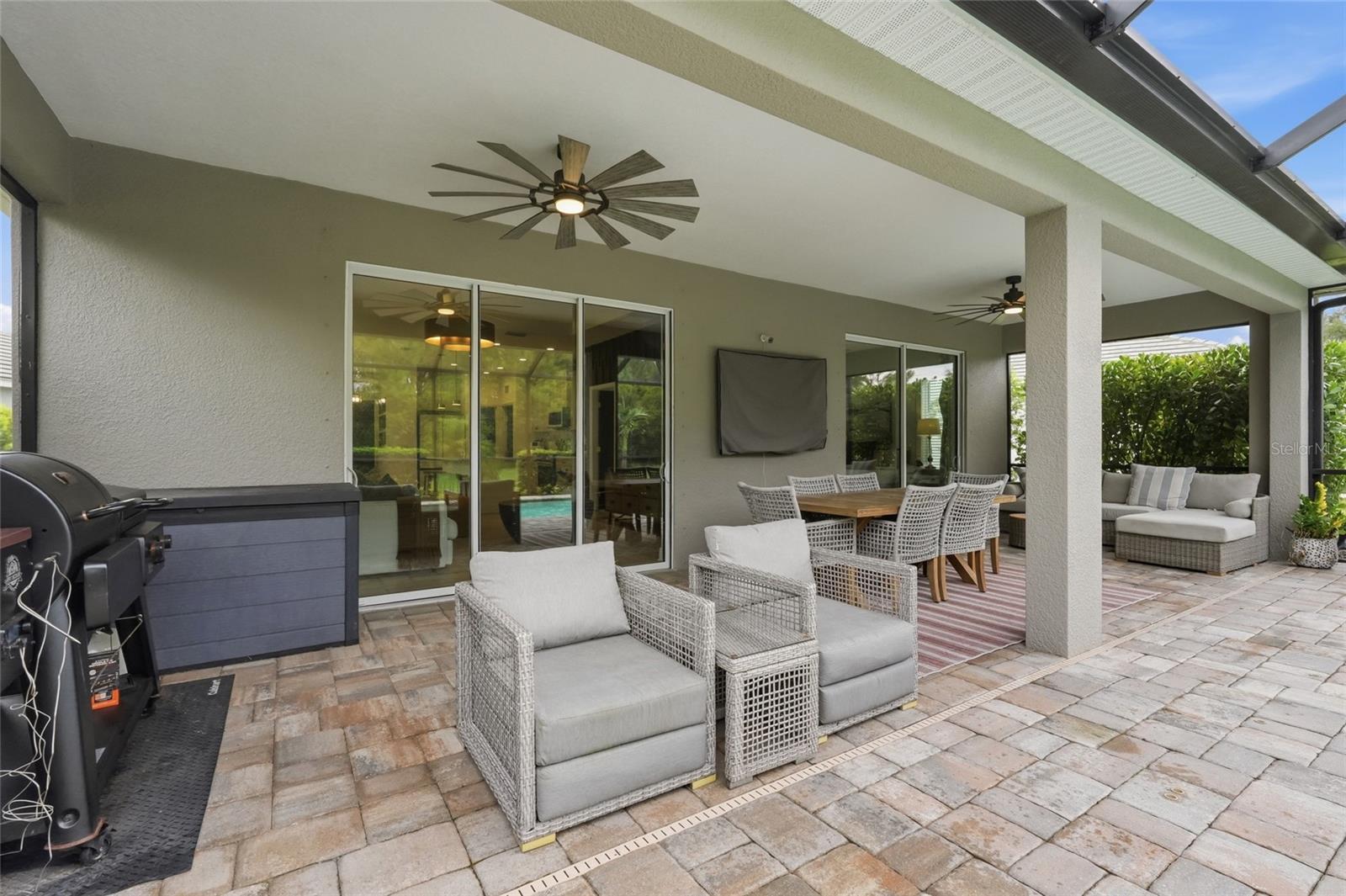 Covered patio with wicker seating, outdoor dining table, ceiling fans, and a barbecue grill.