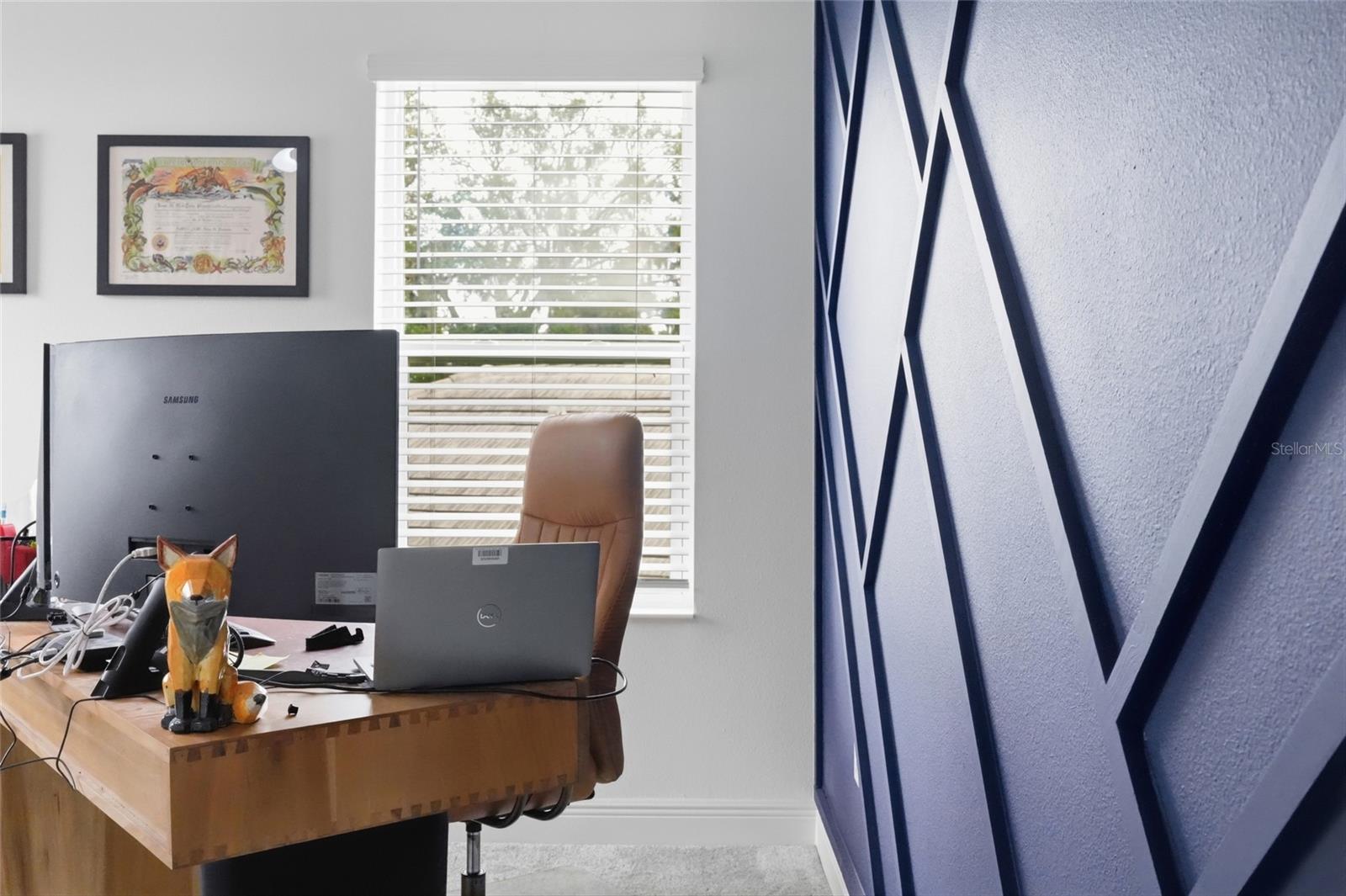 Home office with a wooden desk, computer monitors, and a blue geometric accent wall.