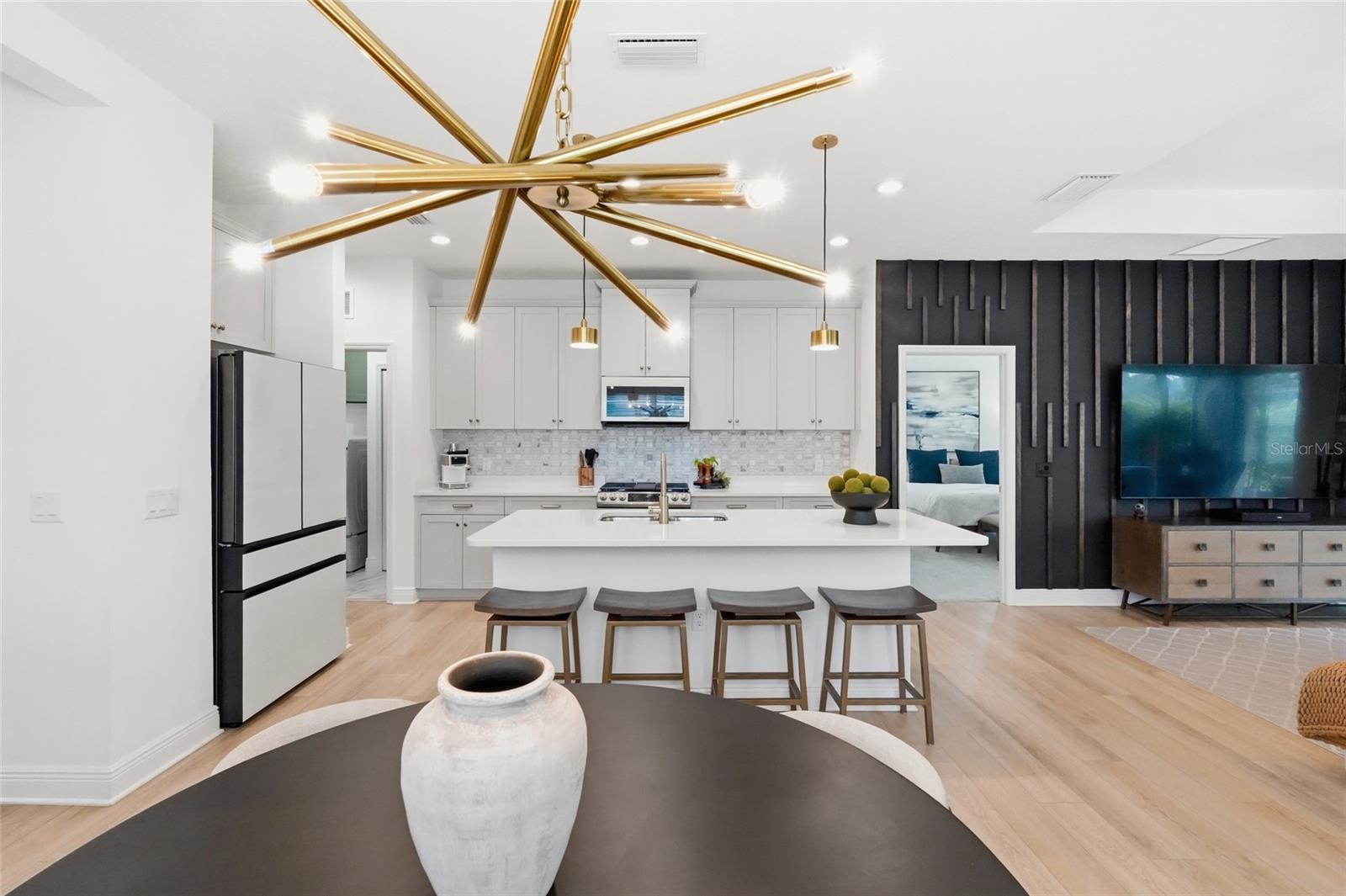 Open-plan kitchen with a white island, four stools, and a gold starburst ceiling light.