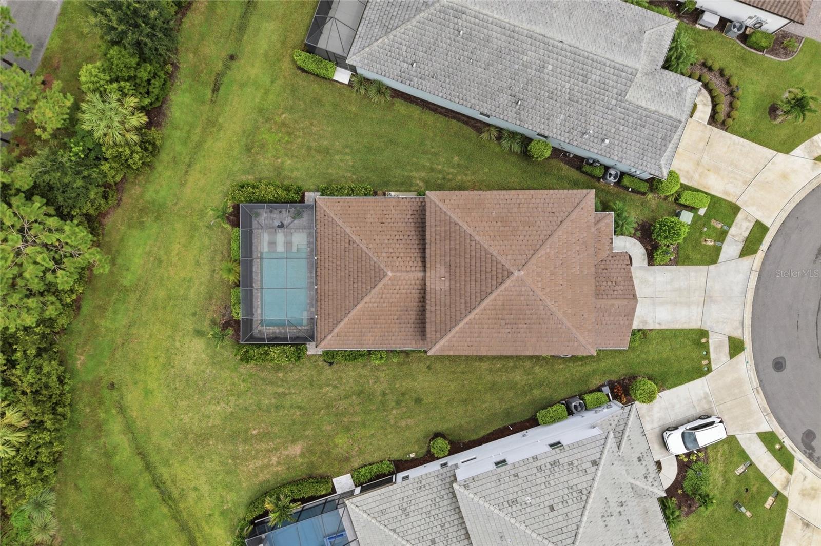 Aerial view of a home with a screened pool, broad lawn, and curved driveway.