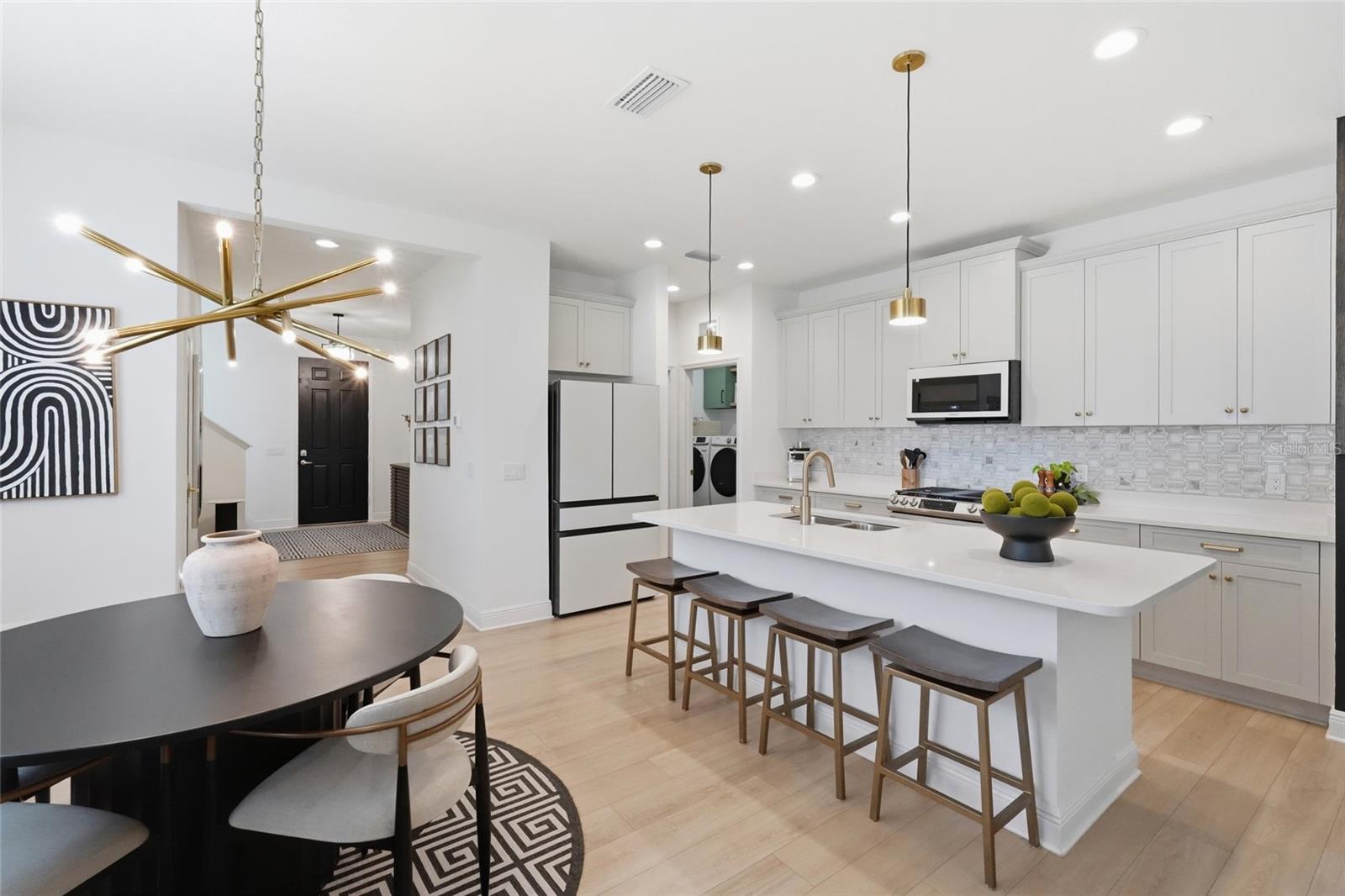 Bright white kitchen with a large island, bar stools, and an adjoining dining area.