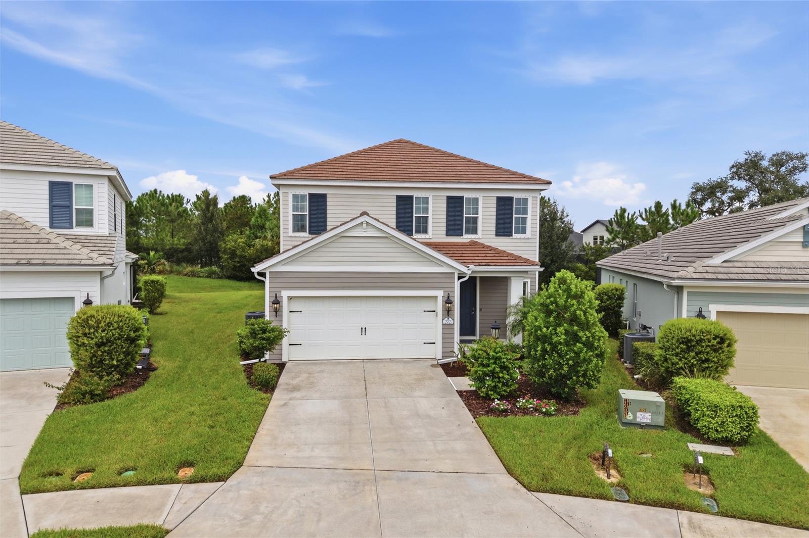 Two-story house with dark shutters, tiled roof, double garage, and landscaped front yard.