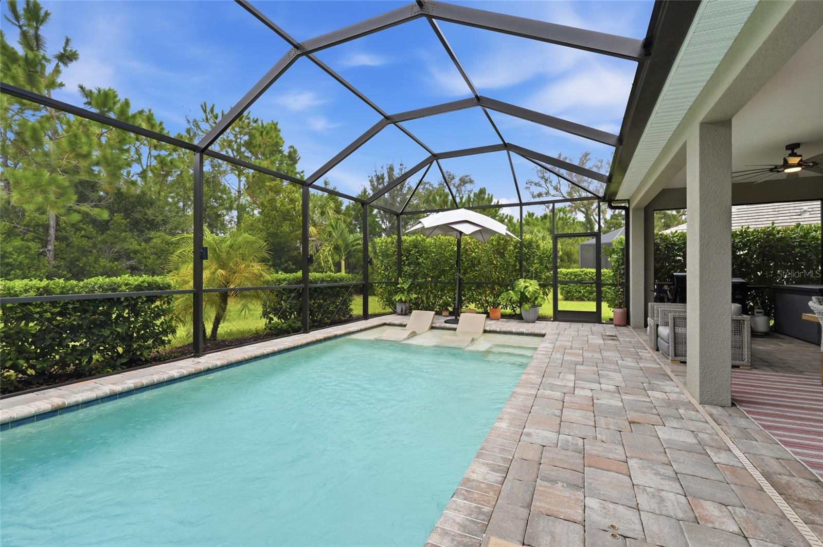 Screened pool lanai with in-water loungers, a paved deck, and covered patio seating.