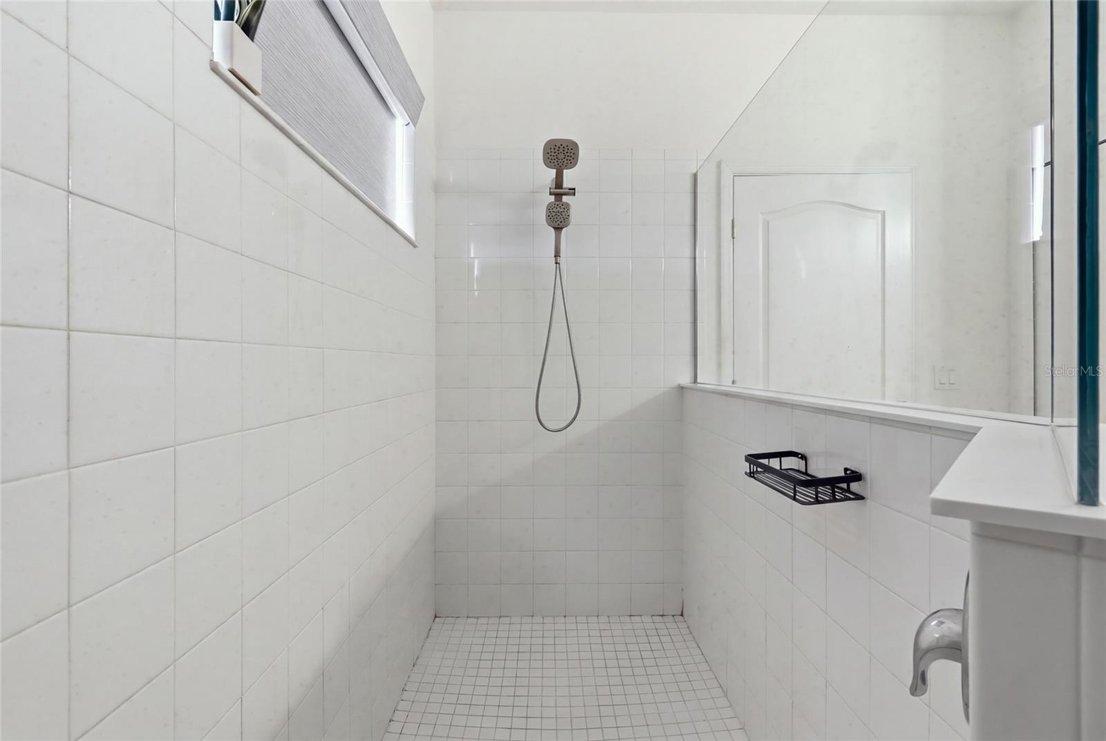 Walk-in shower with white tile, a handheld showerhead, and a glass partition.