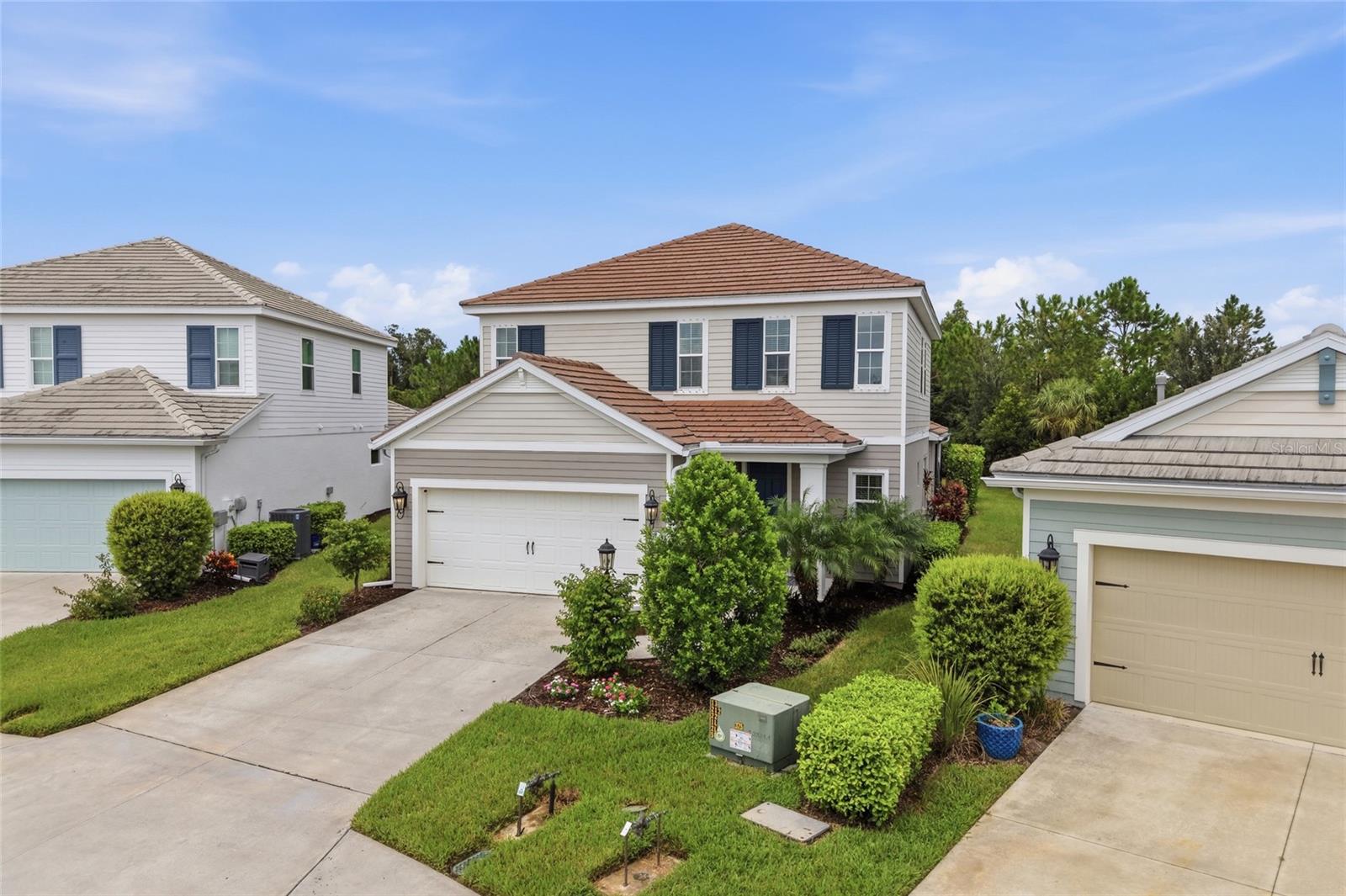 Two-story home with a terracotta tile roof, dark shutters, attached double garage, and landscaped front yard.