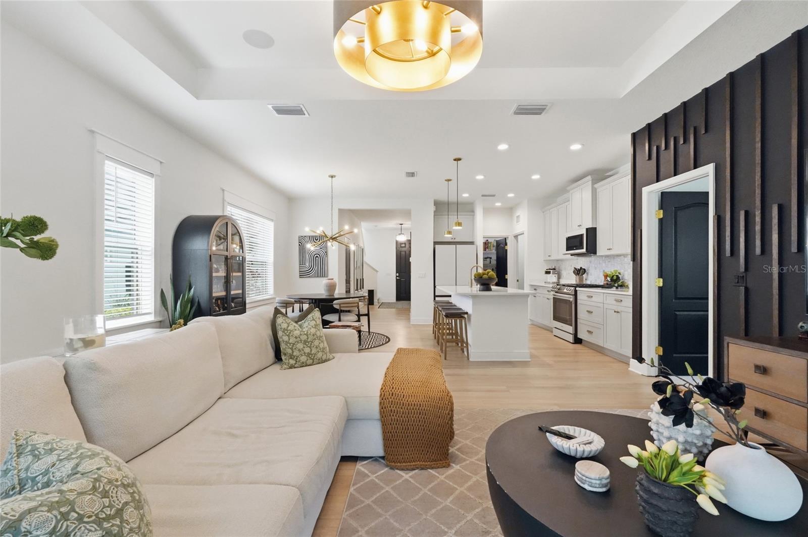 Open-concept living room with a white sectional, dark accent wall, and adjoining kitchen with a large island.