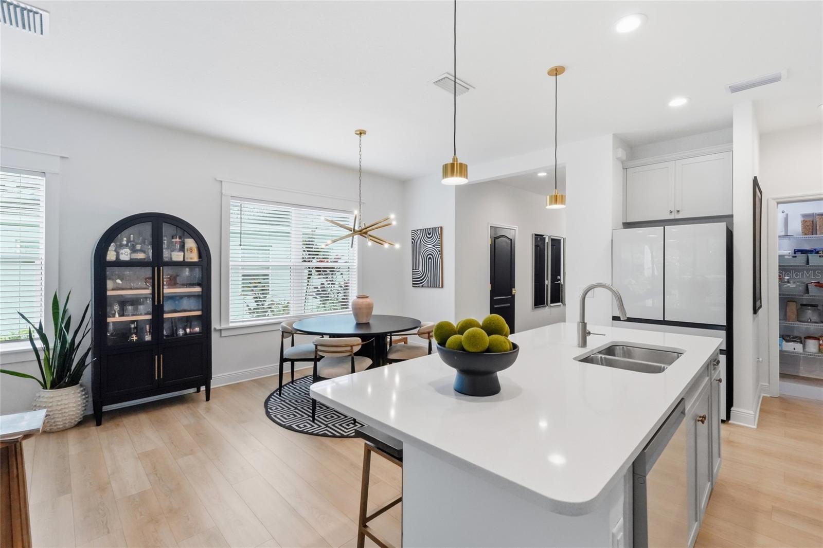 Bright kitchen with a large white island, brass faucet, and dining area beside wide windows.