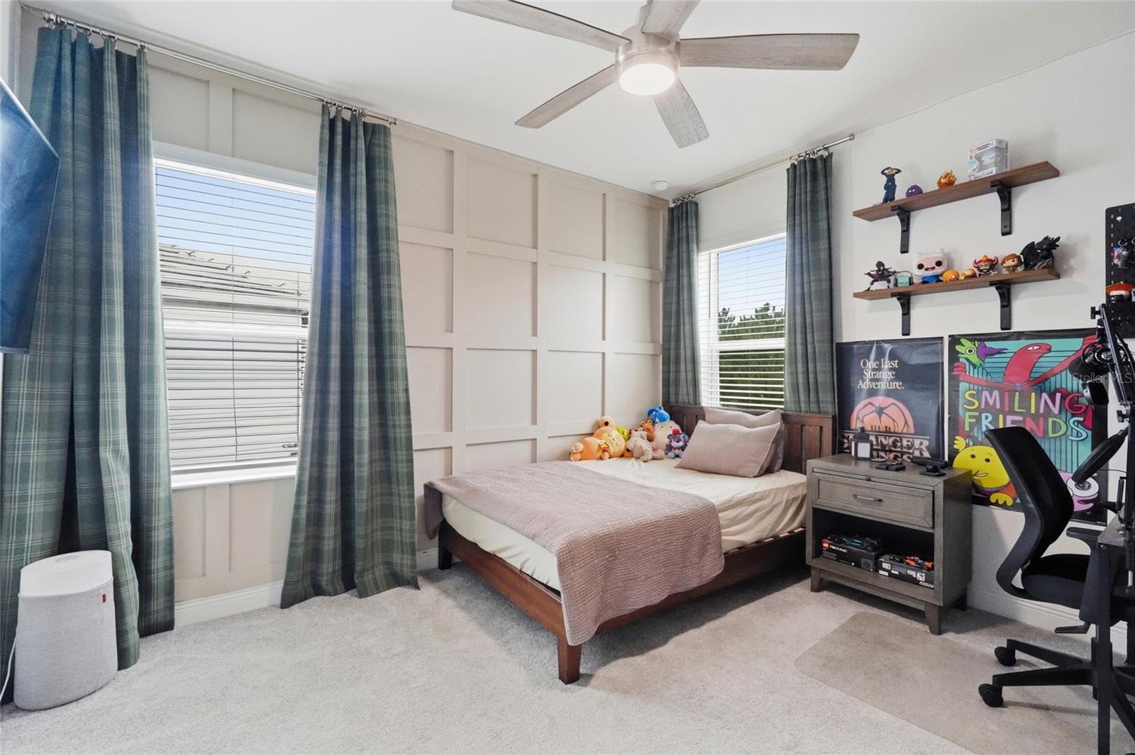 Furnished bedroom with a paneled accent wall, single bed, plaid curtains, and gaming chair.