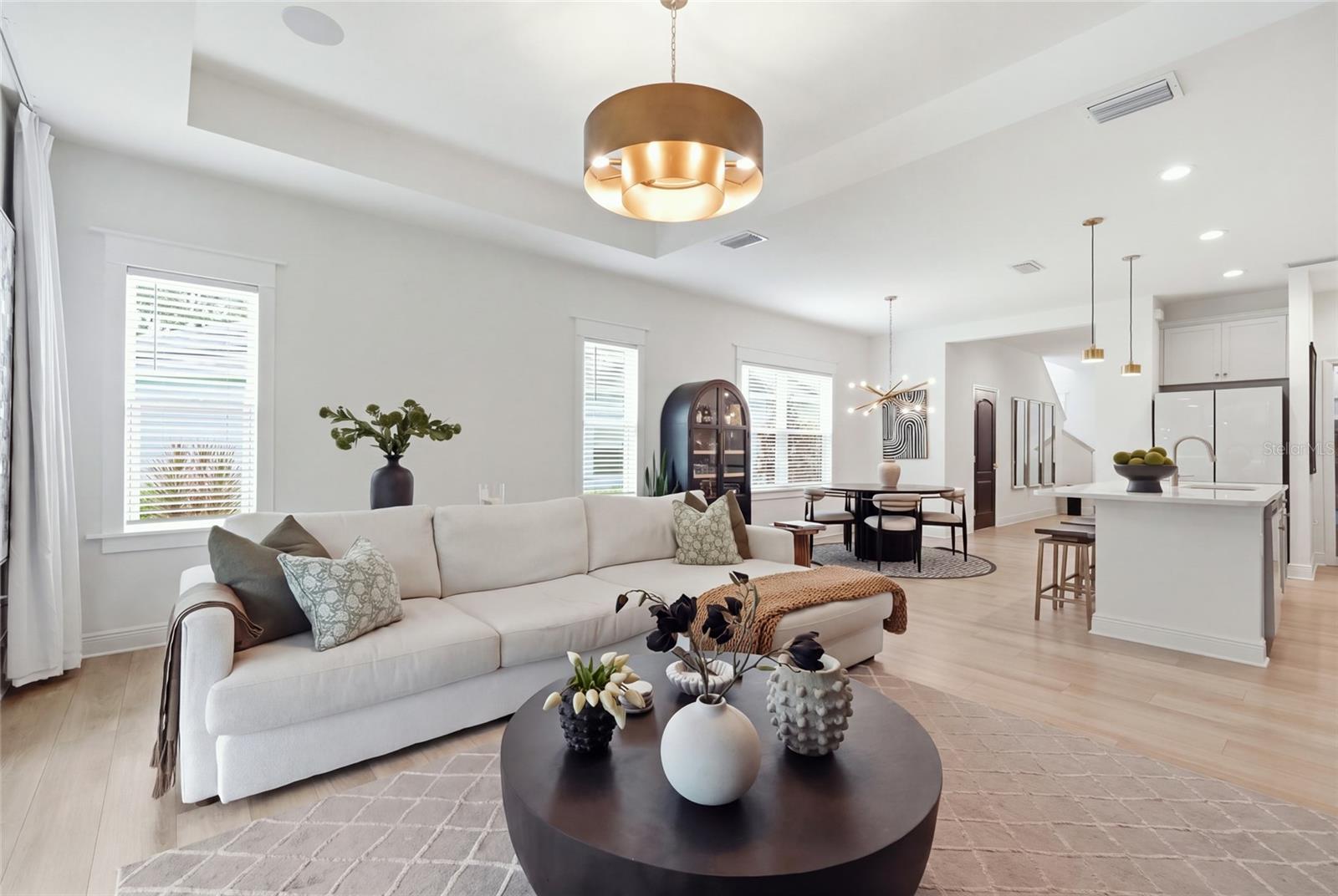 Open-plan living room with white sectional, round coffee table, dining area, and kitchen island.