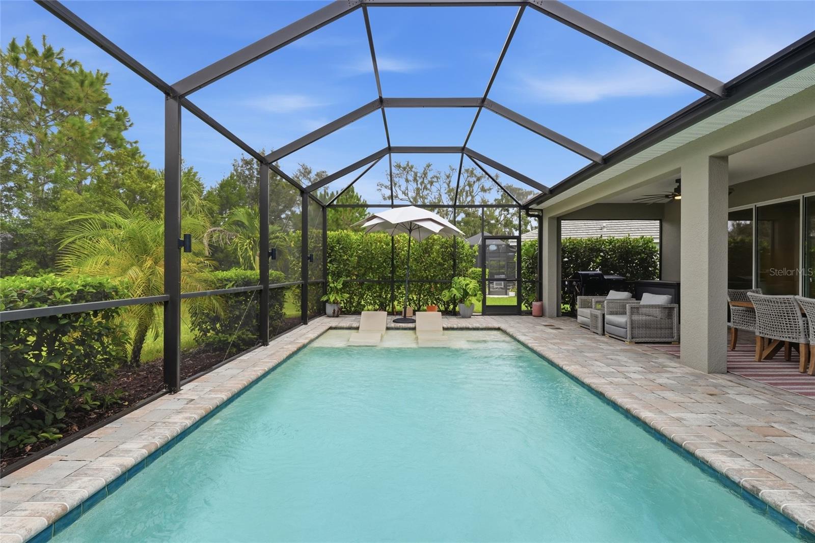 Backyard pool in a screened lanai beside a covered patio with lounge seating.