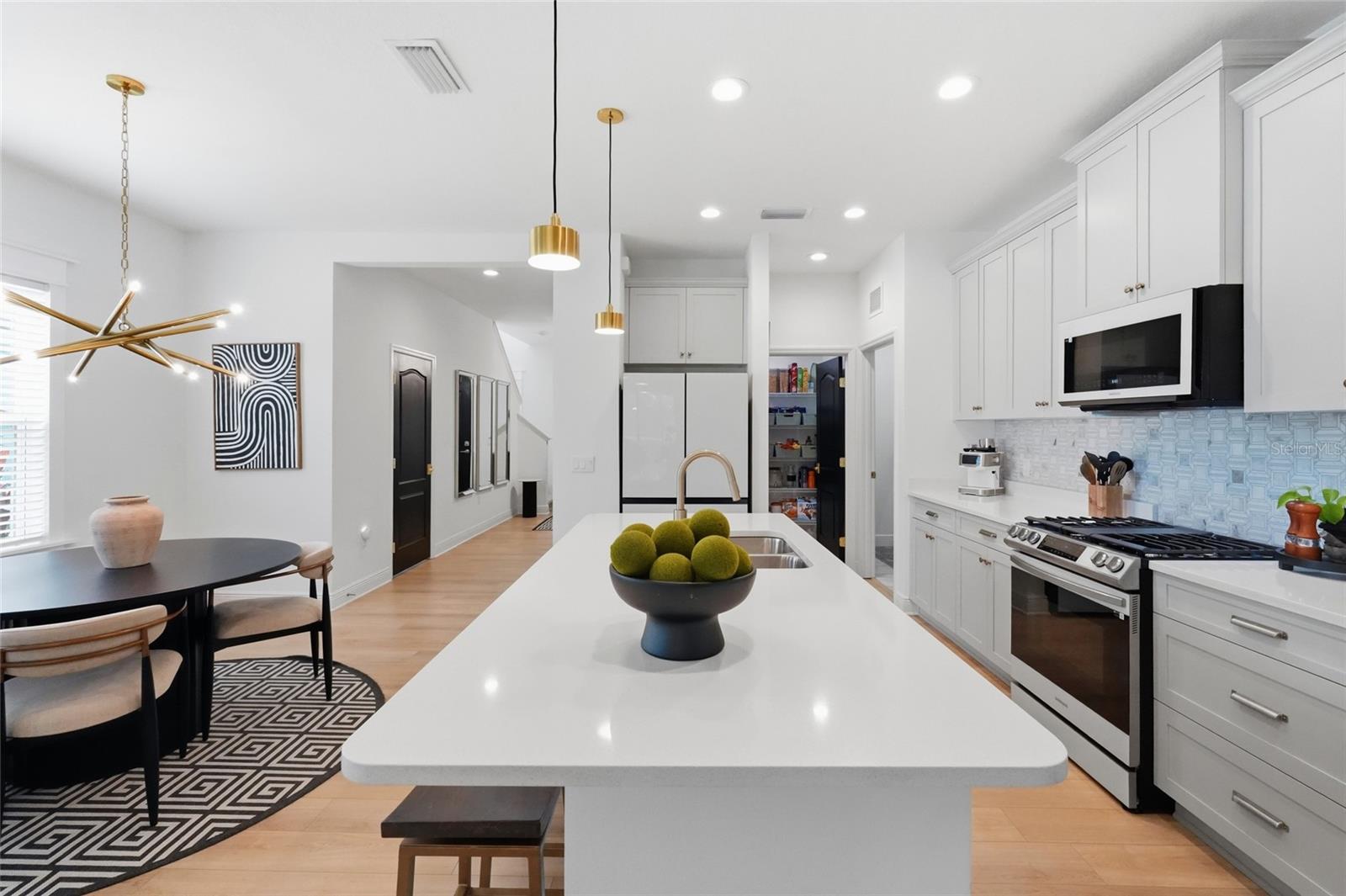 Modern white kitchen with a large island, stainless steel range, and adjoining dining area.
