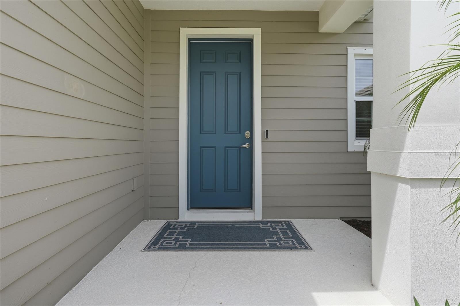Covered home entry with a blue paneled front door and patterned doormat.