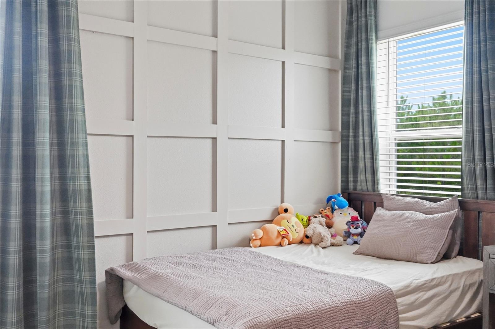 Bedroom with a paneled accent wall, mauve bedding, plush toys, and blue plaid curtains.
