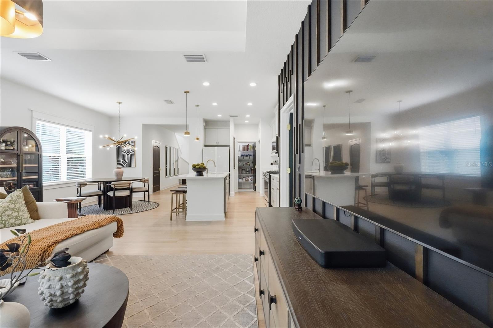 Open-plan living room and kitchen with a white sofa, dining area, island, and large television.