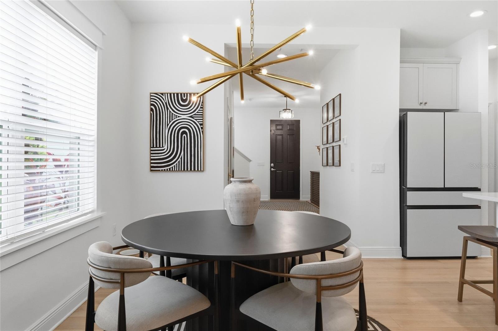 Dining area with a round dark table, upholstered chairs, and a brass starburst chandelier.