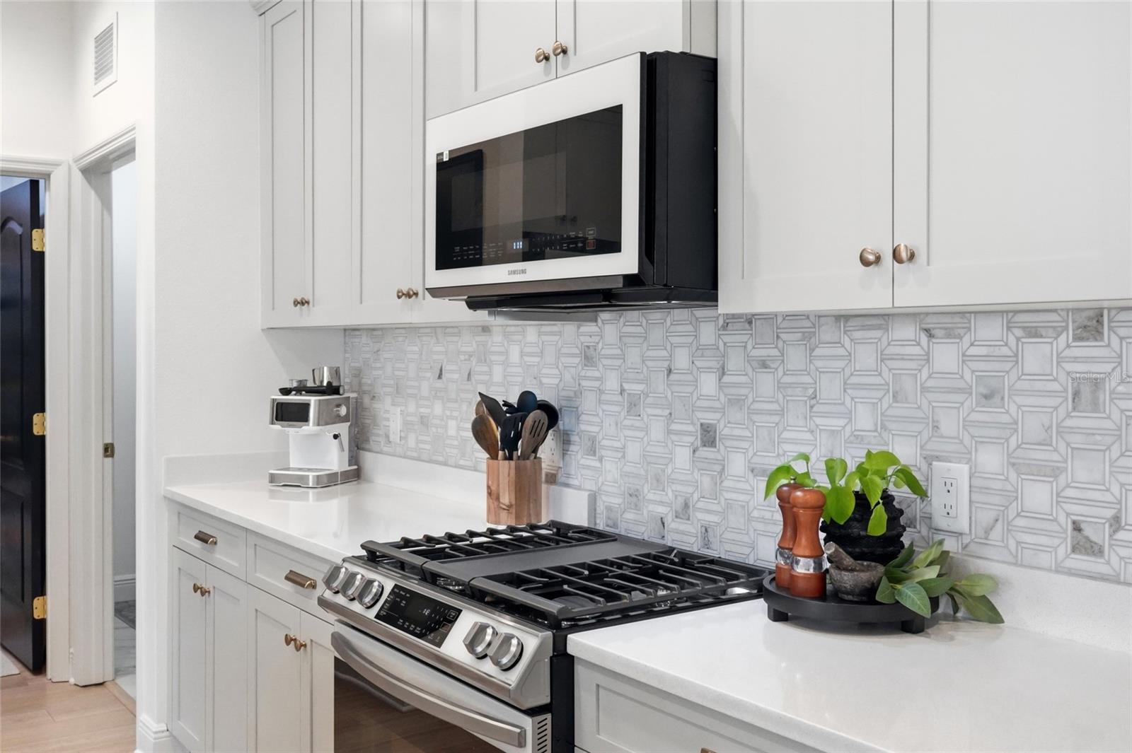 White kitchen with a stainless gas range, geometric tile backsplash, and white cabinets.