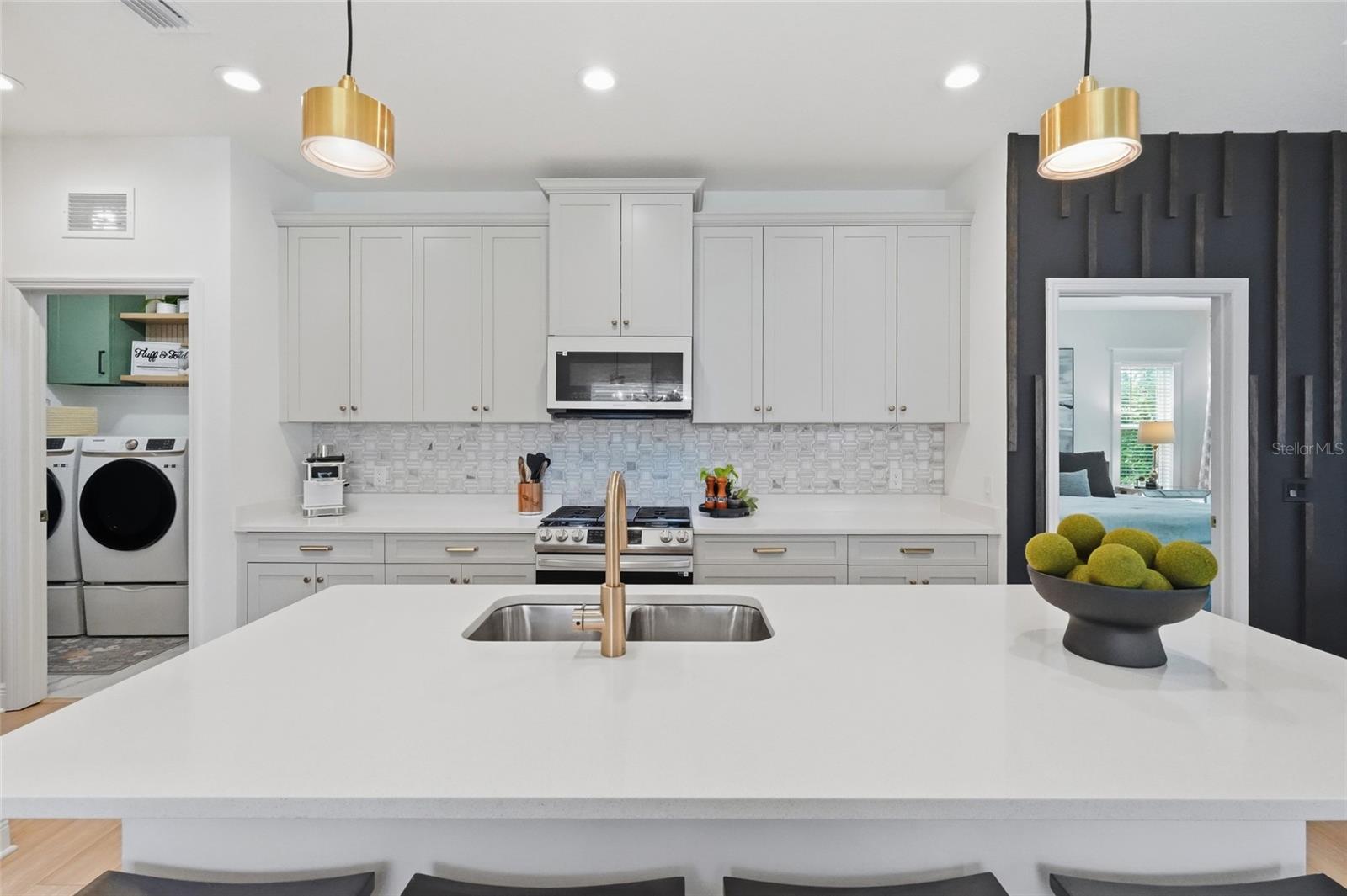 Kitchen with white shaker cabinets, patterned tile backsplash, and a large island with brass faucet.