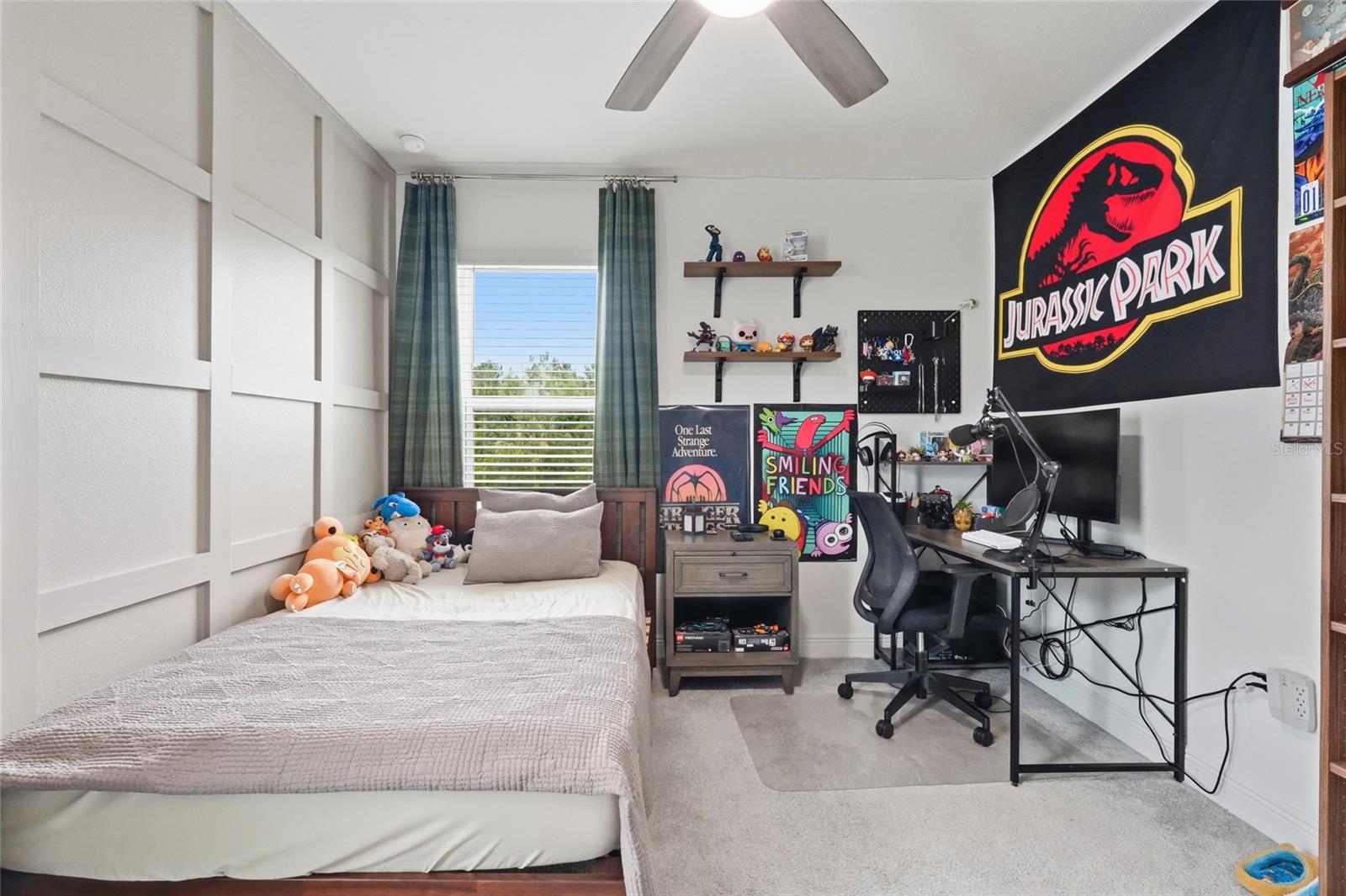 Bedroom with a bed, computer desk, and Jurassic Park banner.