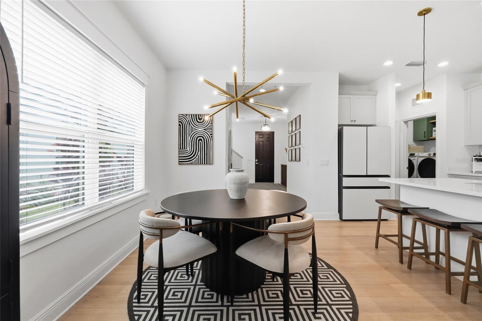 Dining area with a round table, geometric rug, brass chandelier, and open view into the kitchen.