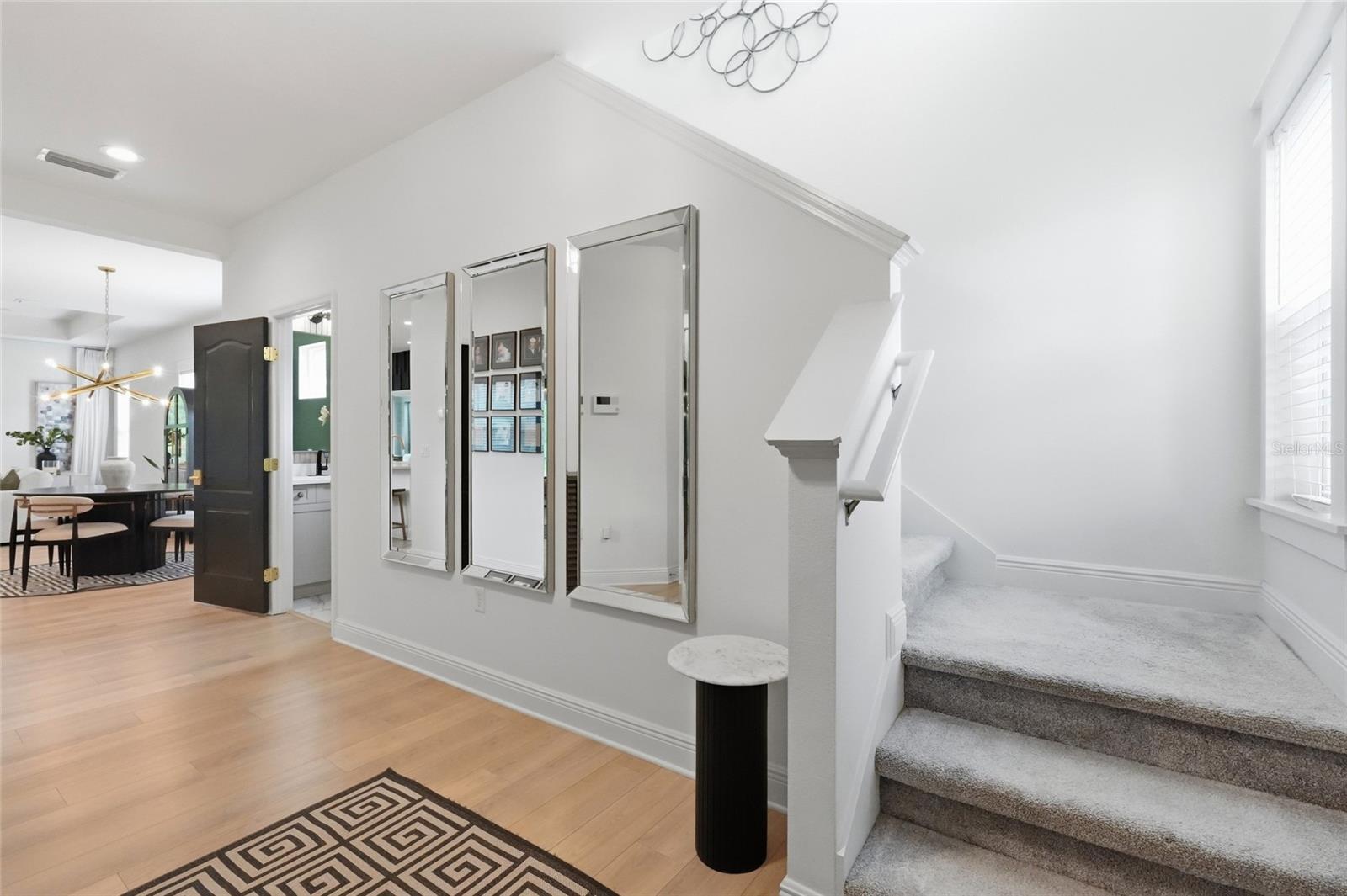 Foyer with mirrored wall, light wood floors, carpeted stairs, and an open view into the dining area.