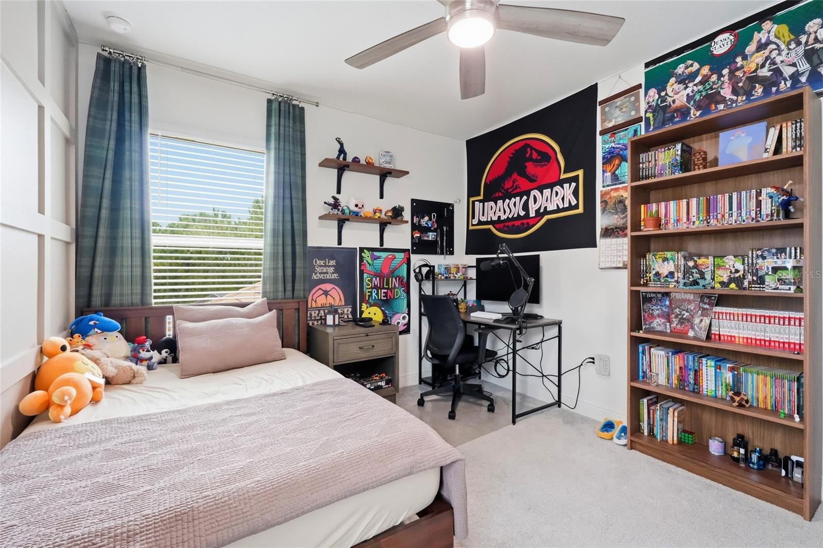 Bedroom with a desk, comic-filled bookcase, and large Jurassic Park banner.