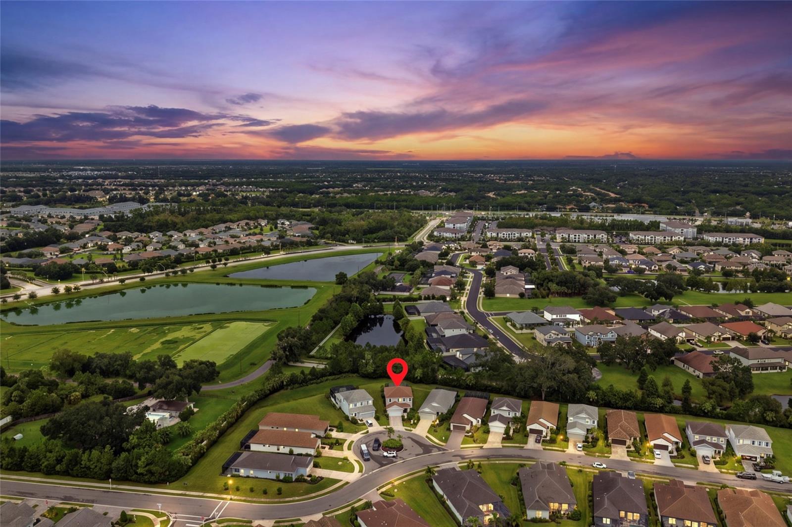 Aerial neighborhood view at dusk, with the property marked by a red pin beside ponds and green space.
