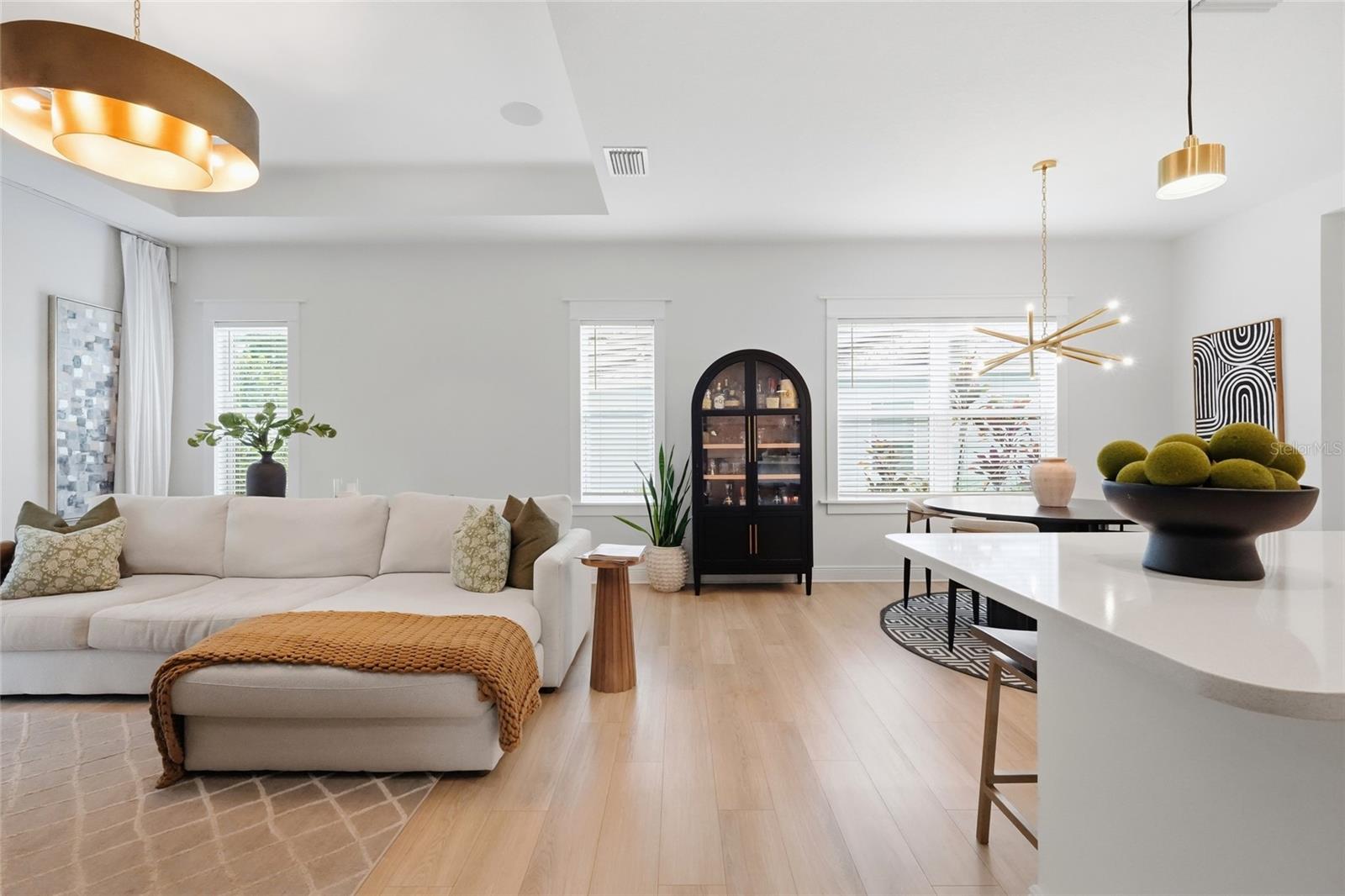 Open-plan living room with a white sectional, pale wood floors, and a black arched display cabinet.