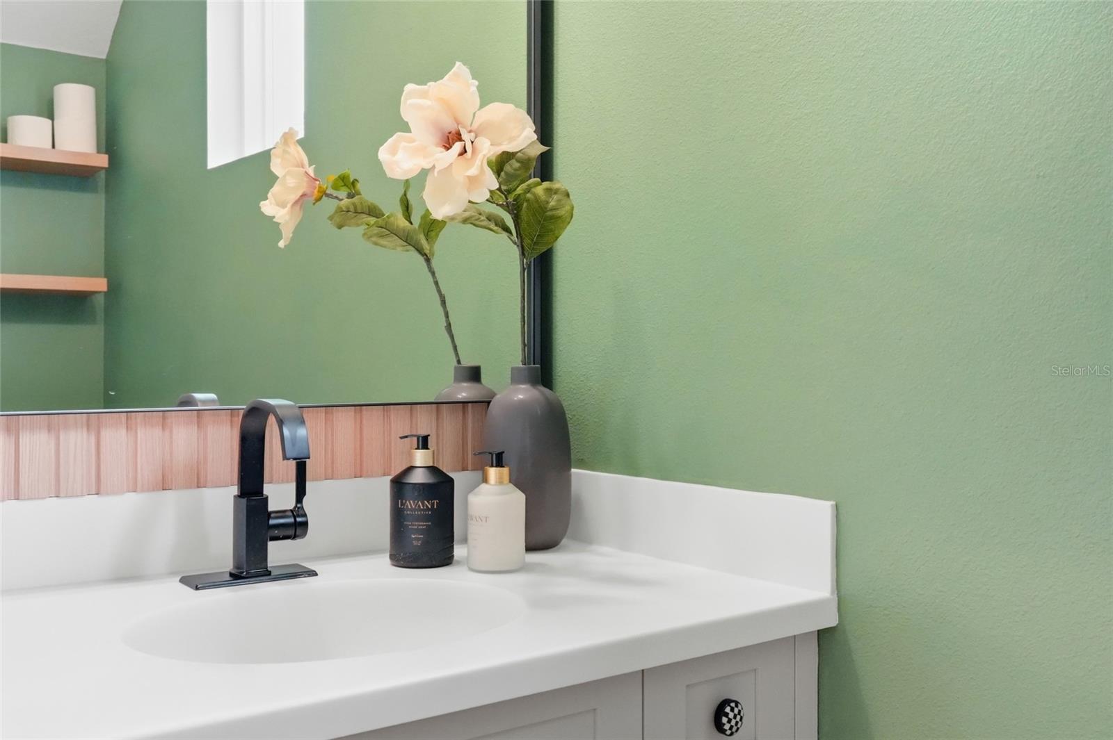 Bathroom vanity with a black faucet, white sink, wood-toned backsplash, and green walls.