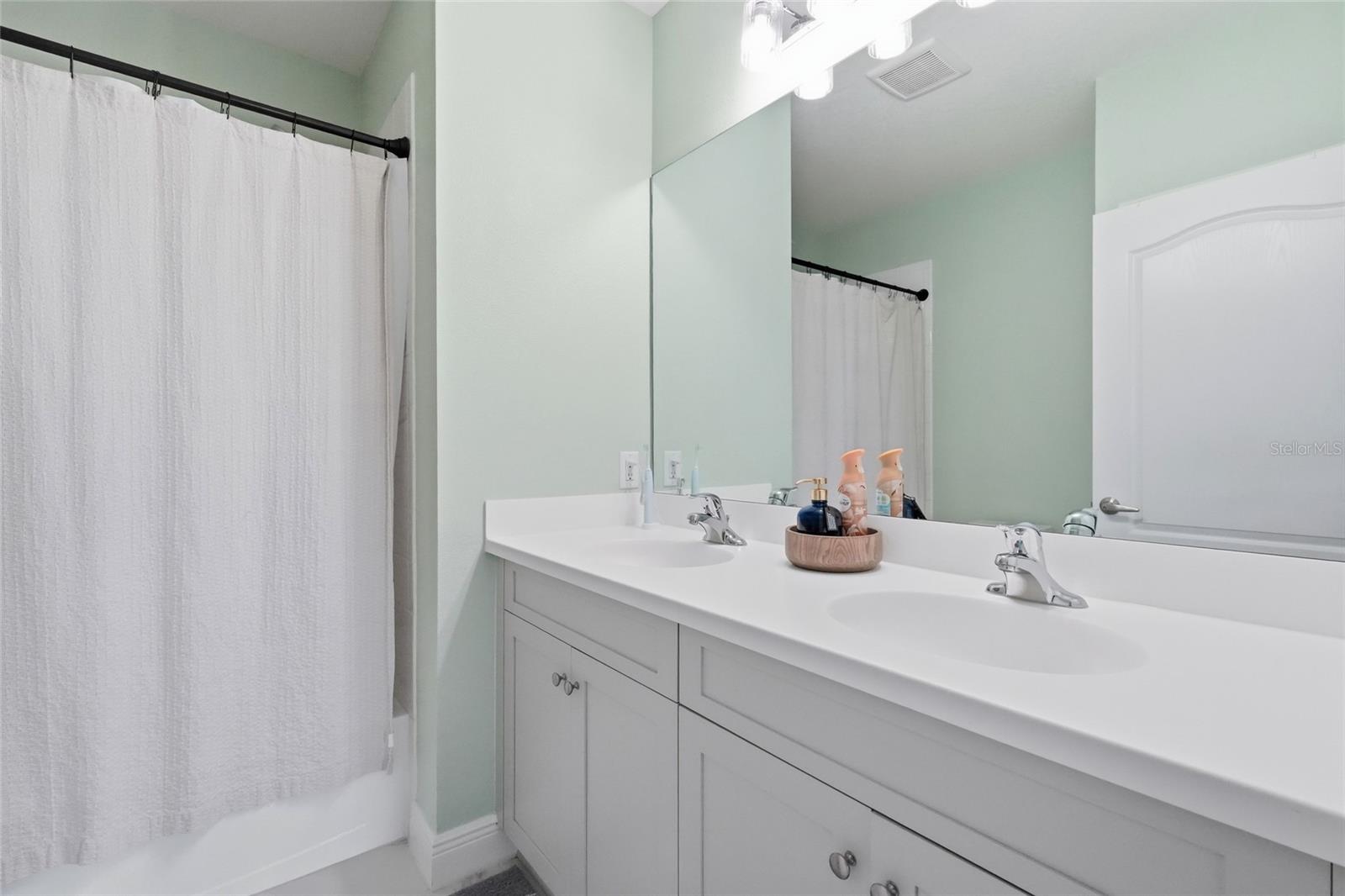 Bathroom with a double-sink vanity and large mirror beside a curtained tub or shower.