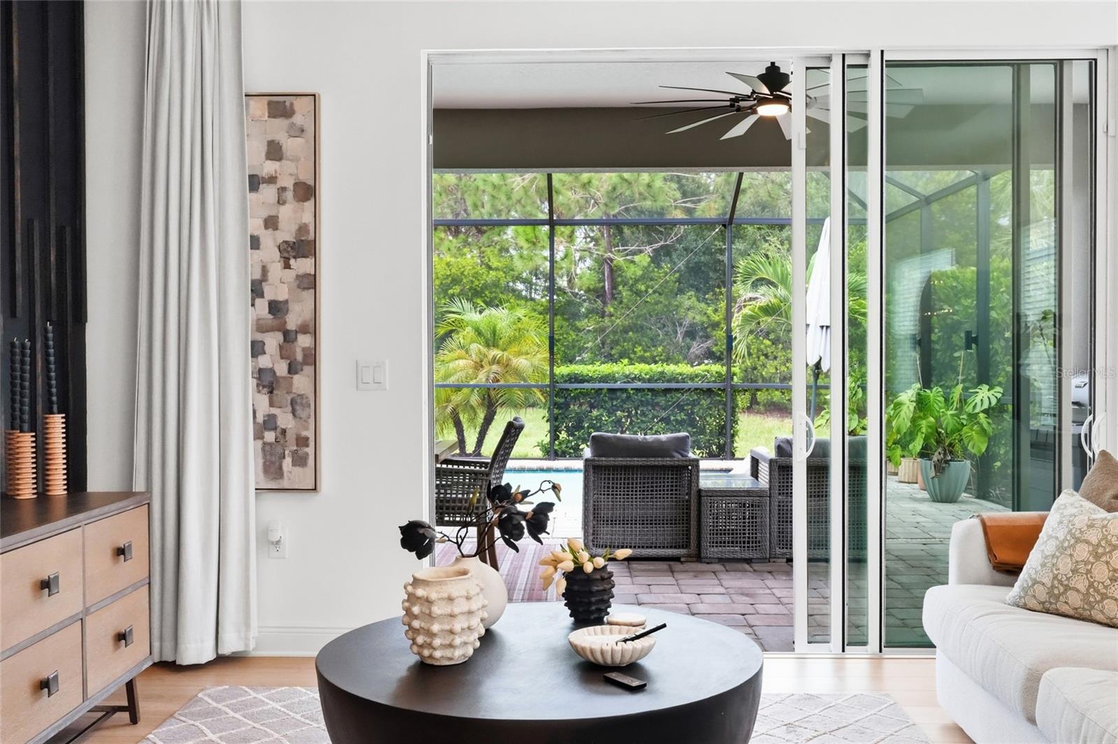Living room with sliding glass doors opening to a screened patio, pool, and lush garden.