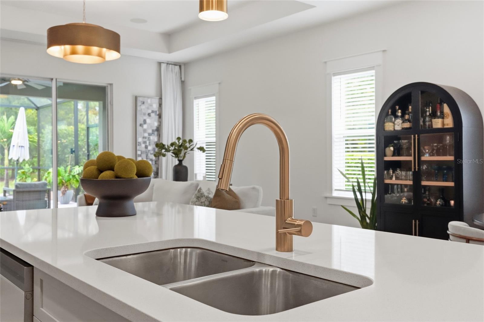 Bright kitchen with a white island, double sink, brass faucet, and black arched bar cabinet.