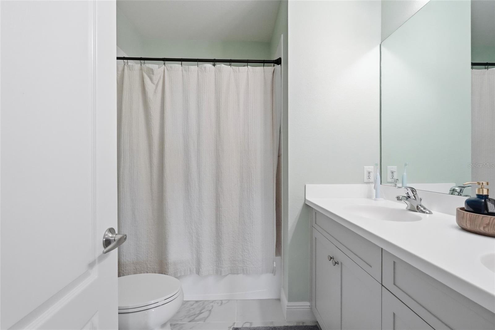 Bathroom with a long double-sink vanity, large mirror, and white shower curtain.