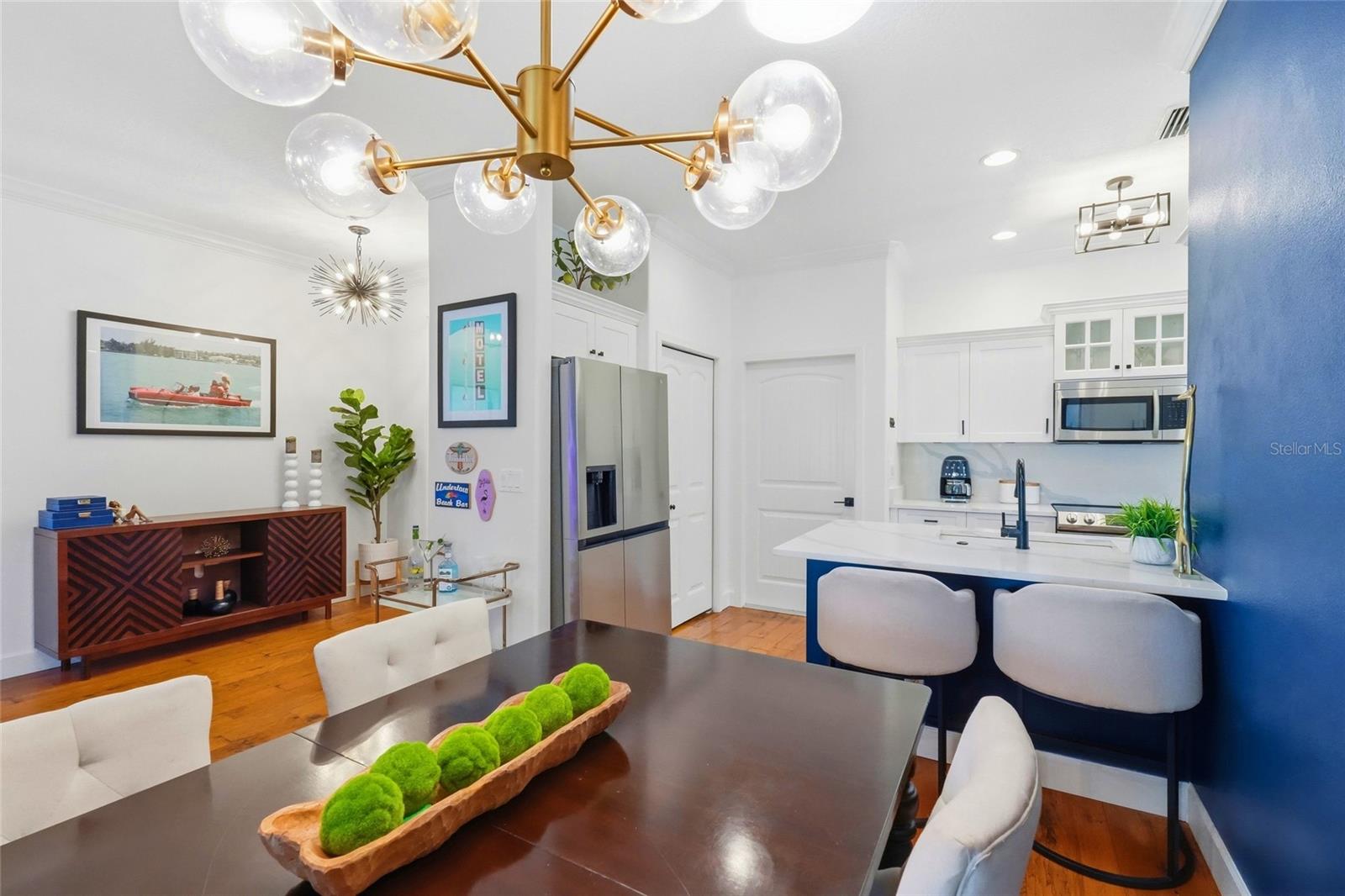 Open-plan kitchen and dining area with a blue island, white cabinetry, and brass globe chandelier.