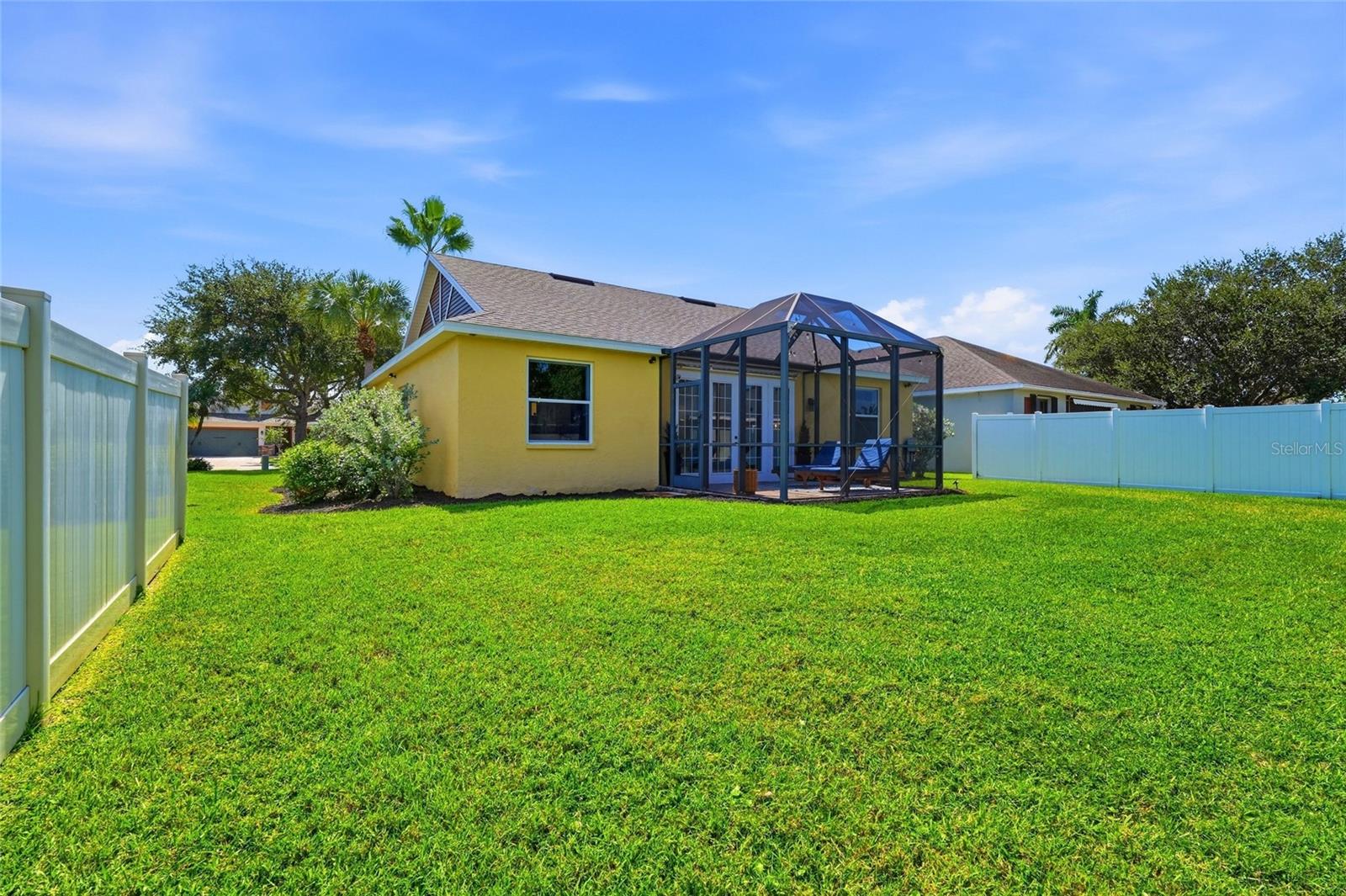 Yellow home with a screened patio, broad green lawn, and white privacy fencing.