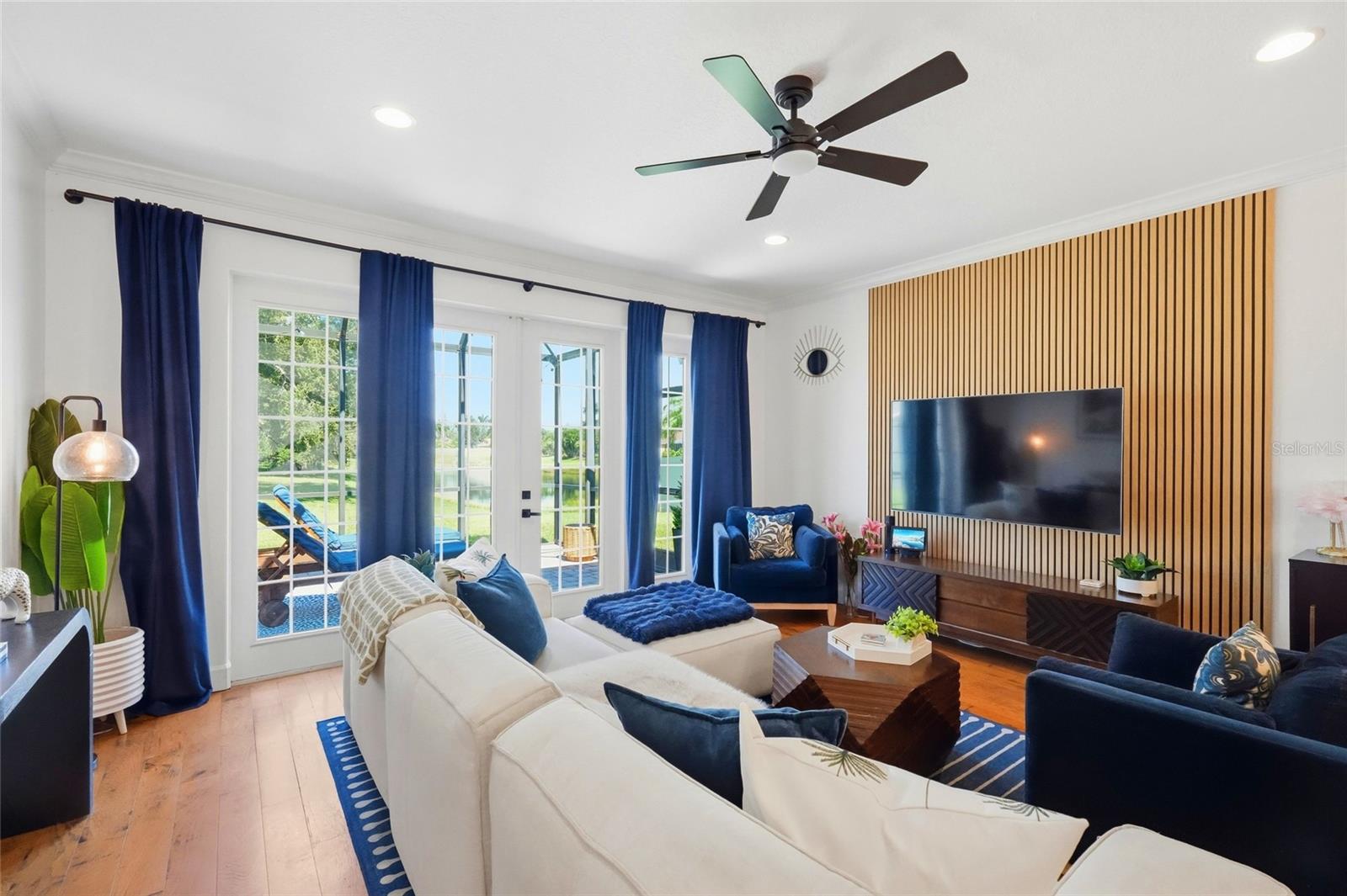 Living room with a wood-slat TV wall, navy seating, and sliding doors overlooking water.