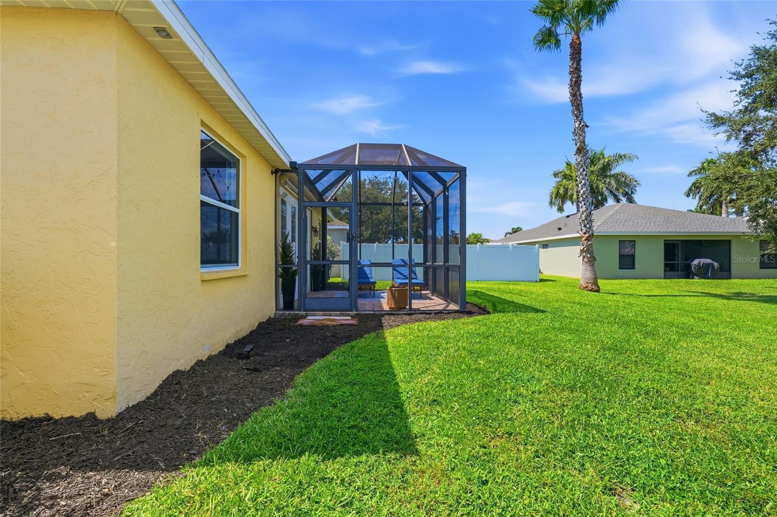 Yellow stucco home with a furnished screened lanai, green lawn, and palm trees.