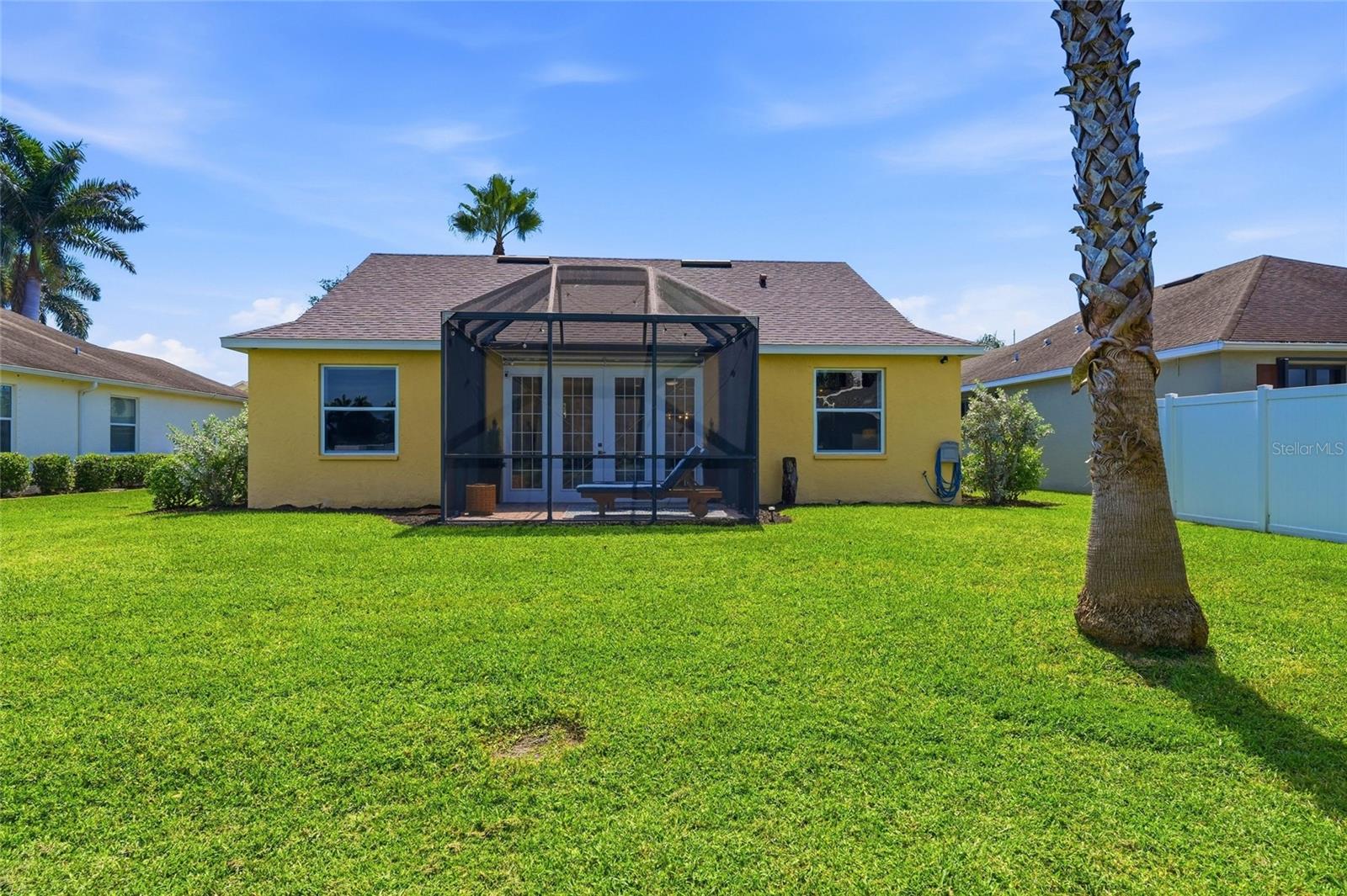 Yellow home’s rear exterior with a screened lanai, broad lawn, and palm tree.
