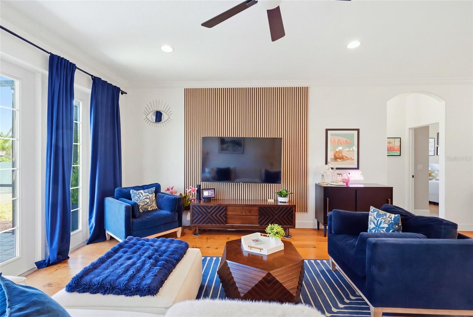 Living room with navy sofas, a television on a wood-slat feature wall, and tall windows with blue curtains.